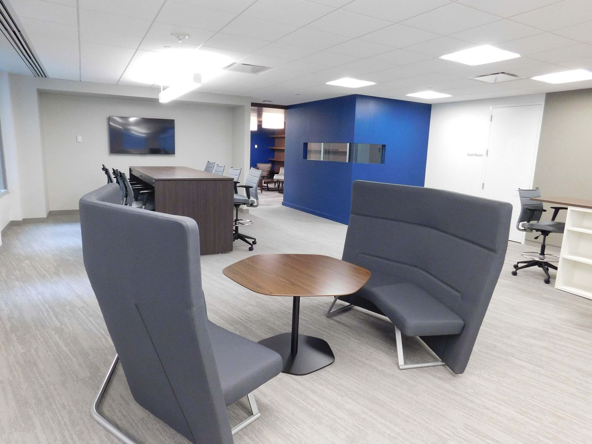Modern office lounge with gray chairs, round table, blue accent wall, and TV screen