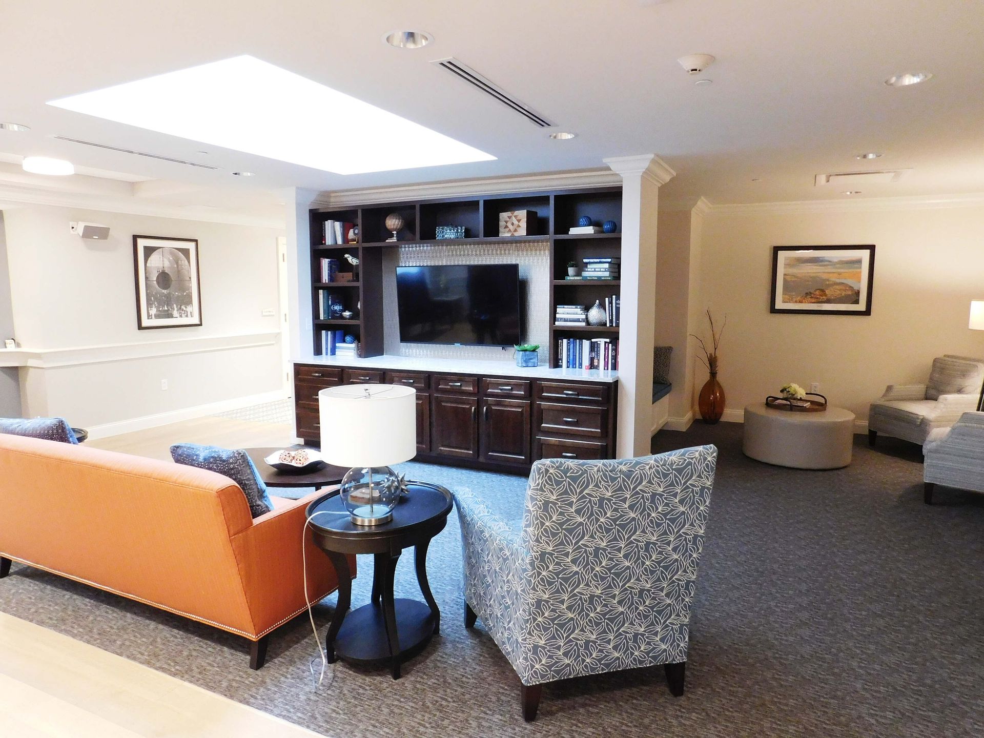 Bright living room with orange sofa, patterned chair, TV wall unit, and neutral decor