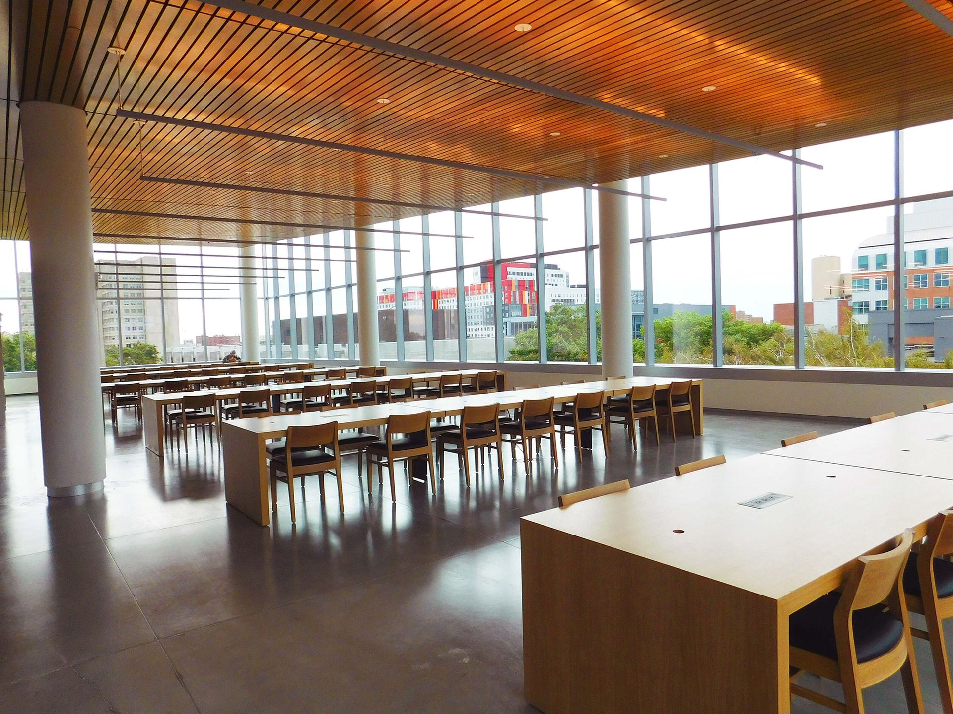 Empty modern cafeteria with long tables, large windows, and a wood-slatted ceiling.