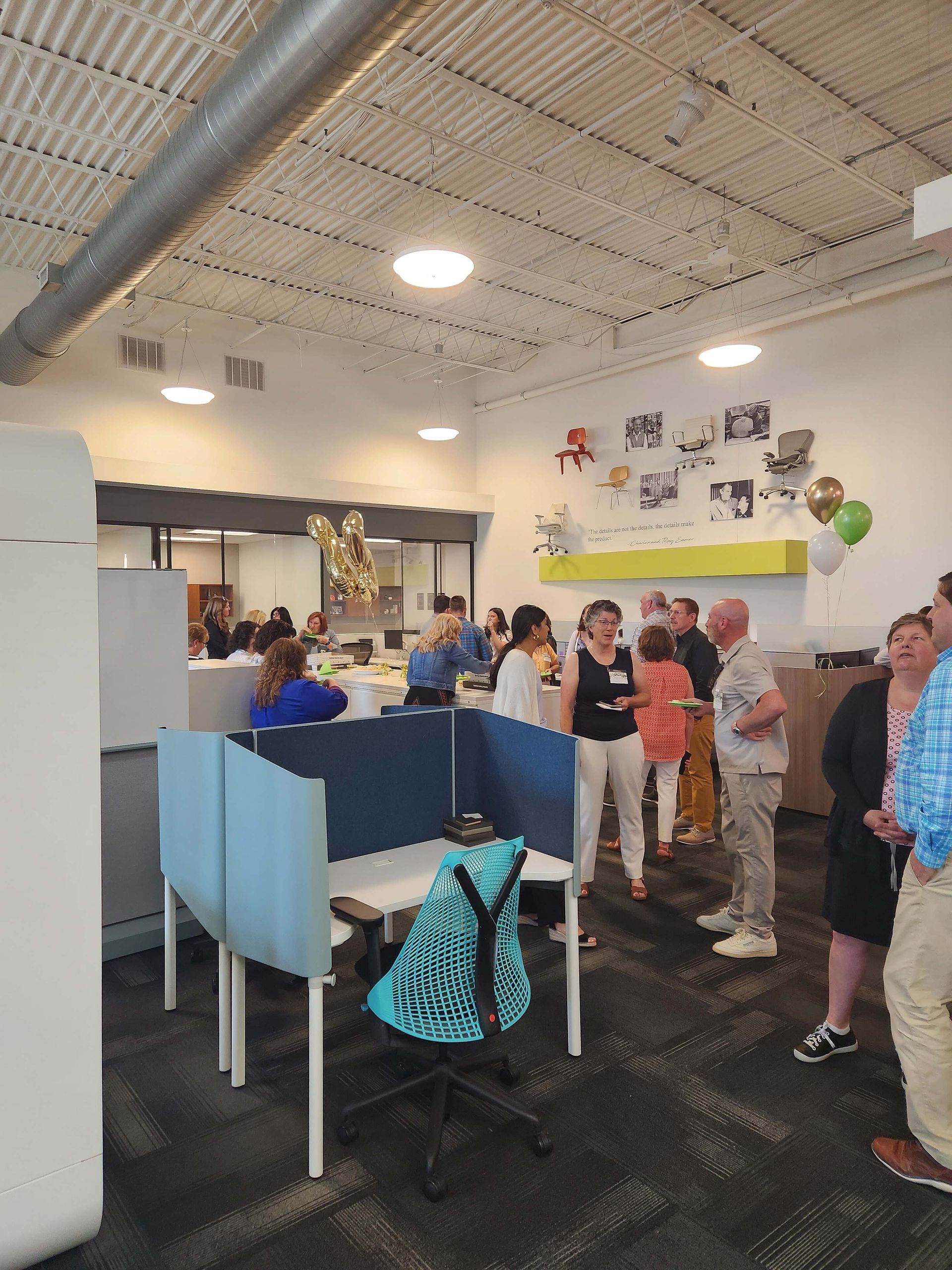 Indoor reception area with people standing near a counter and blue partitions under bright ceiling lights.
