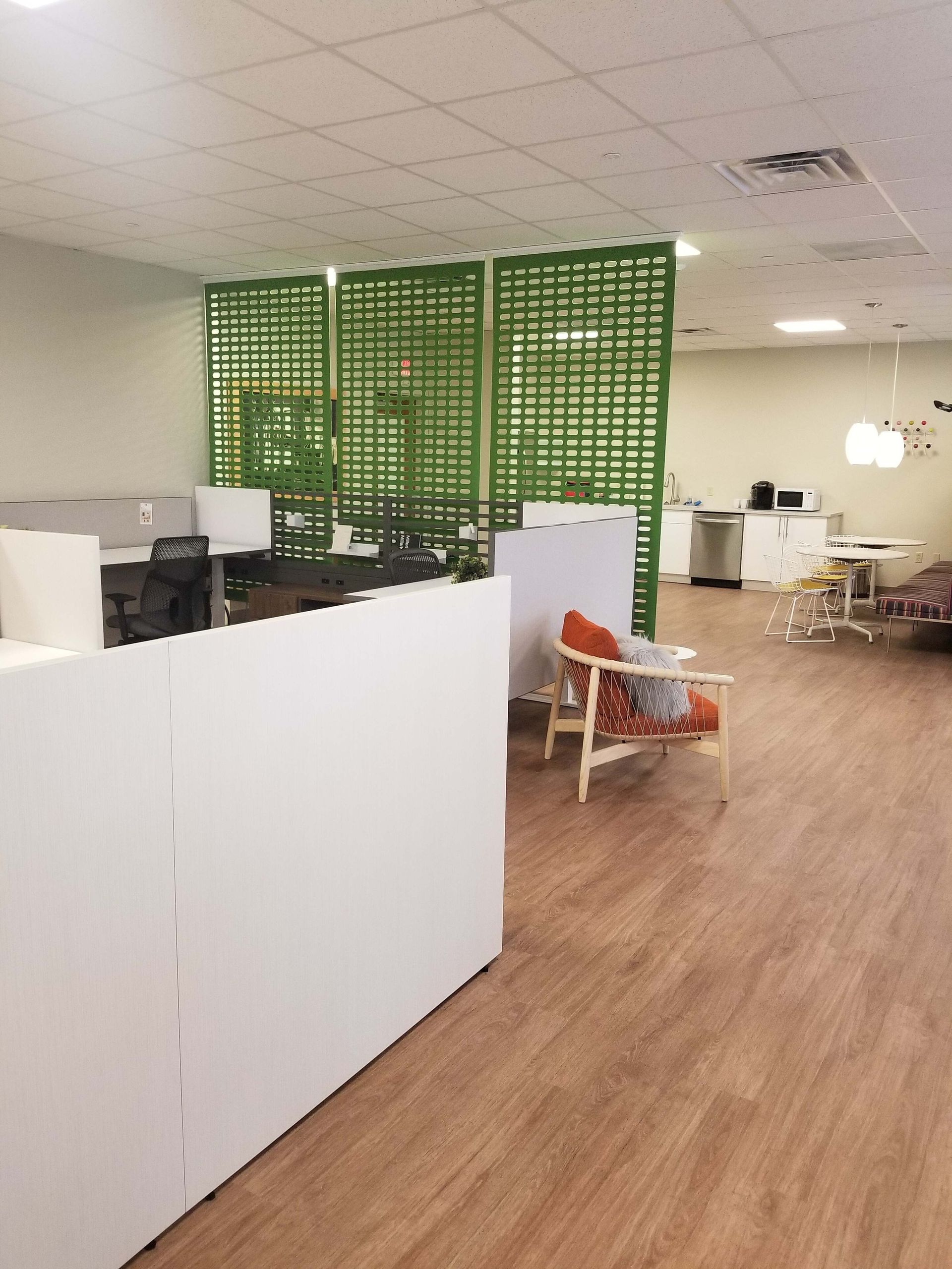 Open office interior with white partitions, wood floor, green divider, and desks under bright ceiling lights