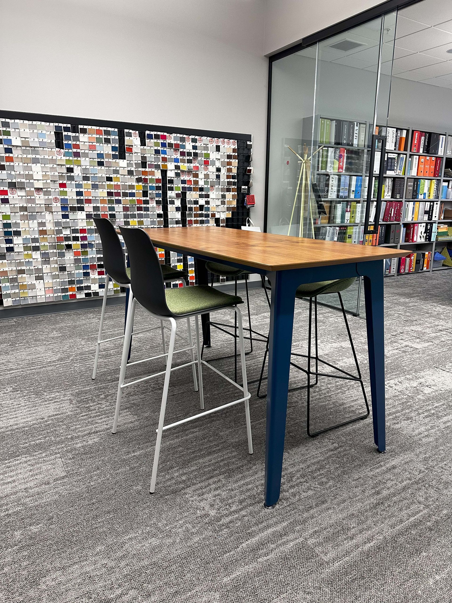 Modern office lounge with a high wooden table, stools, and a wall of colorful notes behind glass cabinets