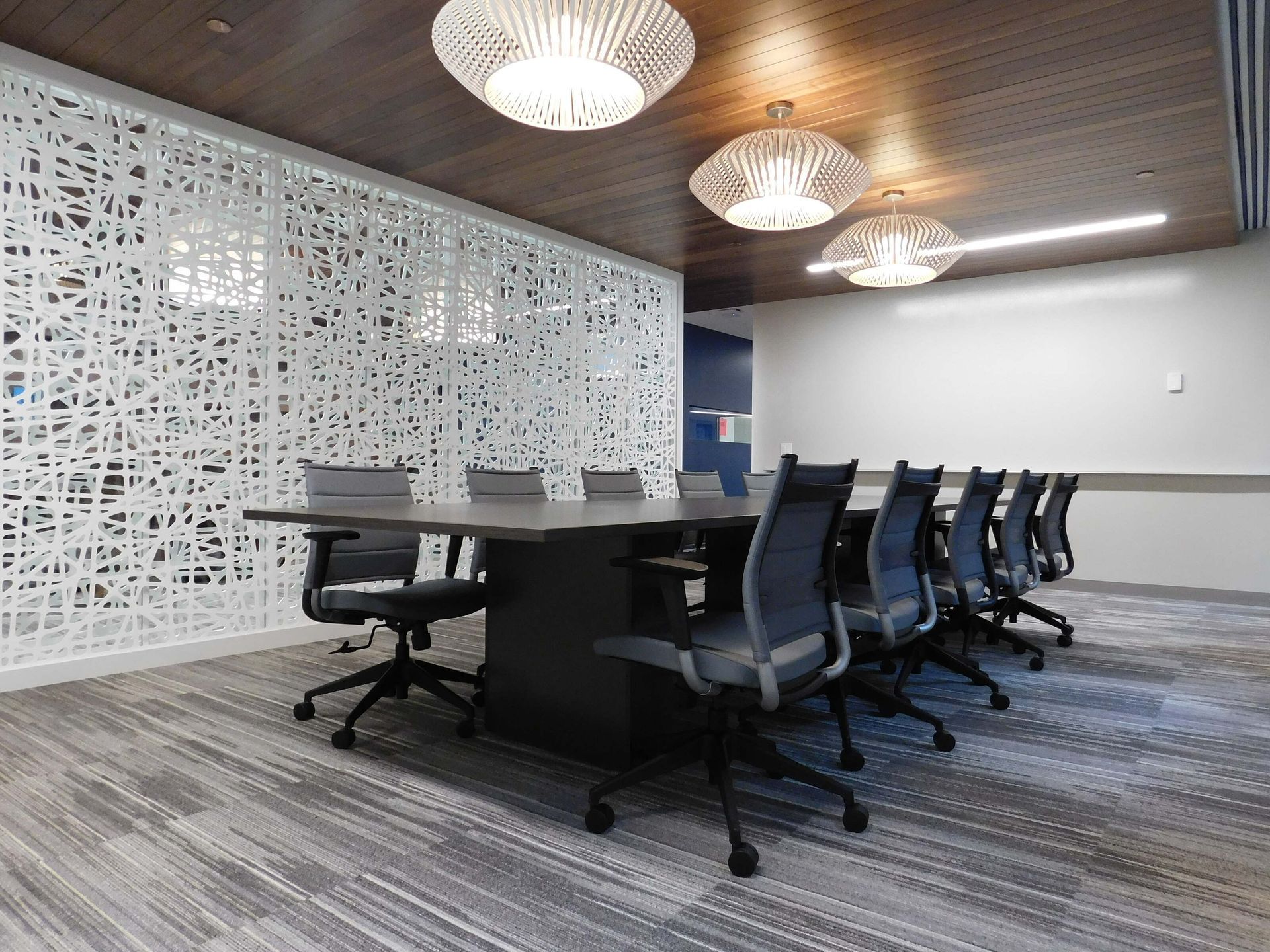 Modern conference room with black chairs, long table, patterned white wall, and wood ceiling lights