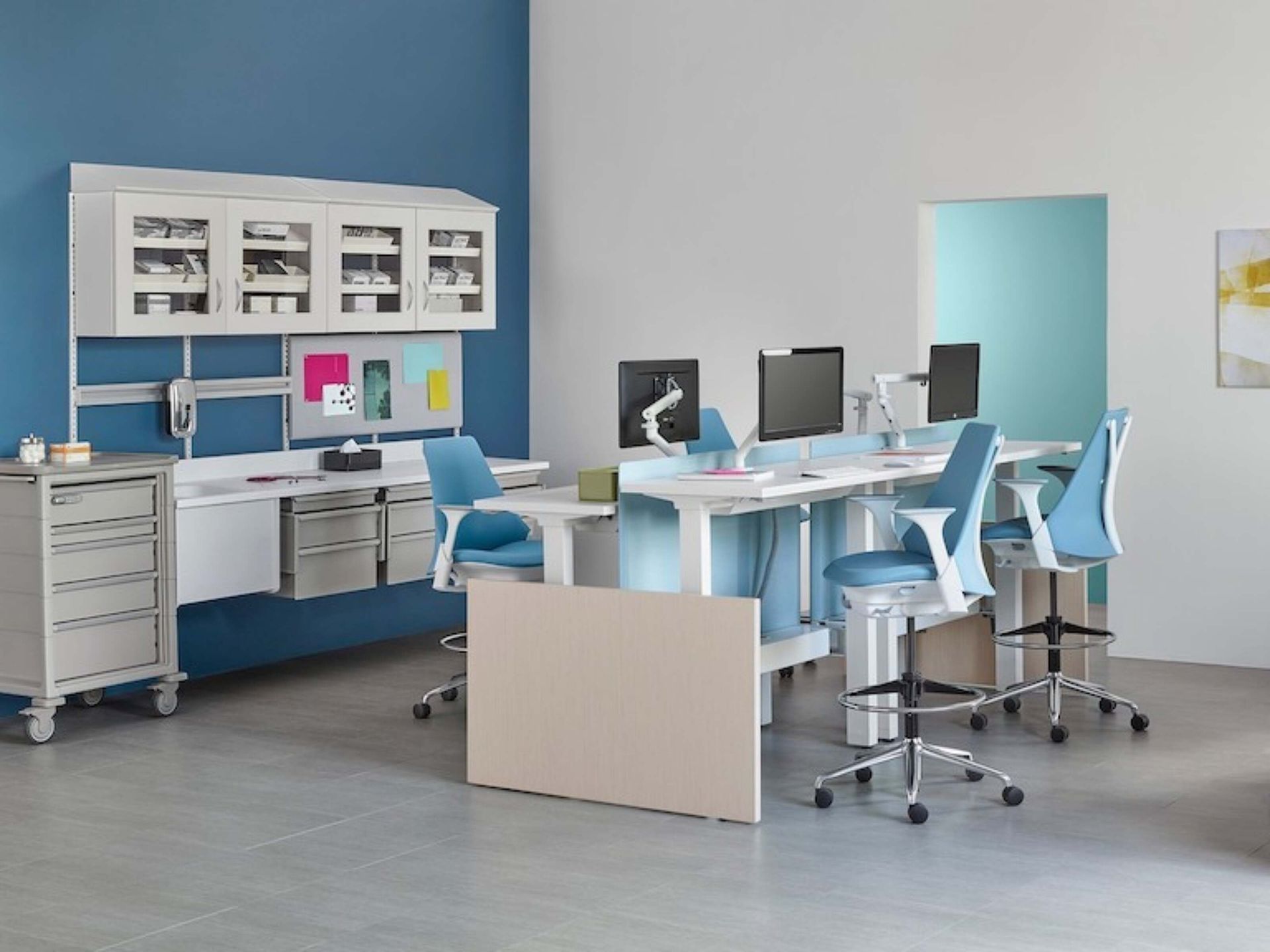 Modern office with white desks, blue chairs, computer monitors, and storage cabinets