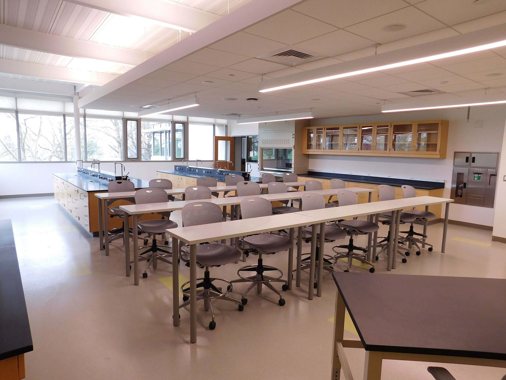 Empty science classroom with lab tables, stools, and cabinets under bright overhead lights