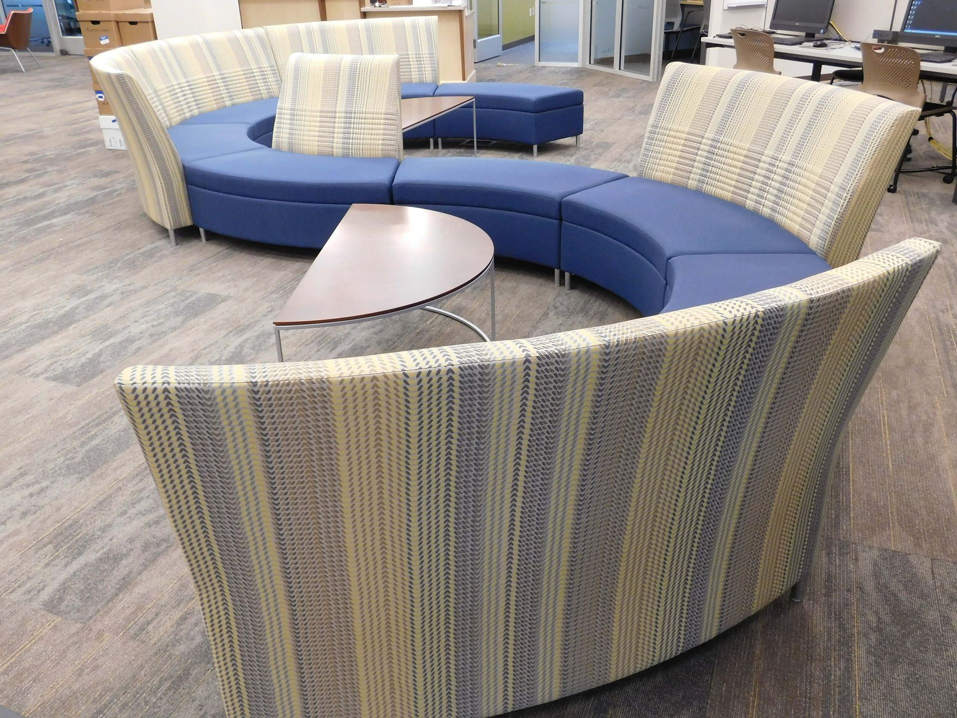 Curved blue-and-tan modular lounge seating with small tables in a carpeted indoor lobby
