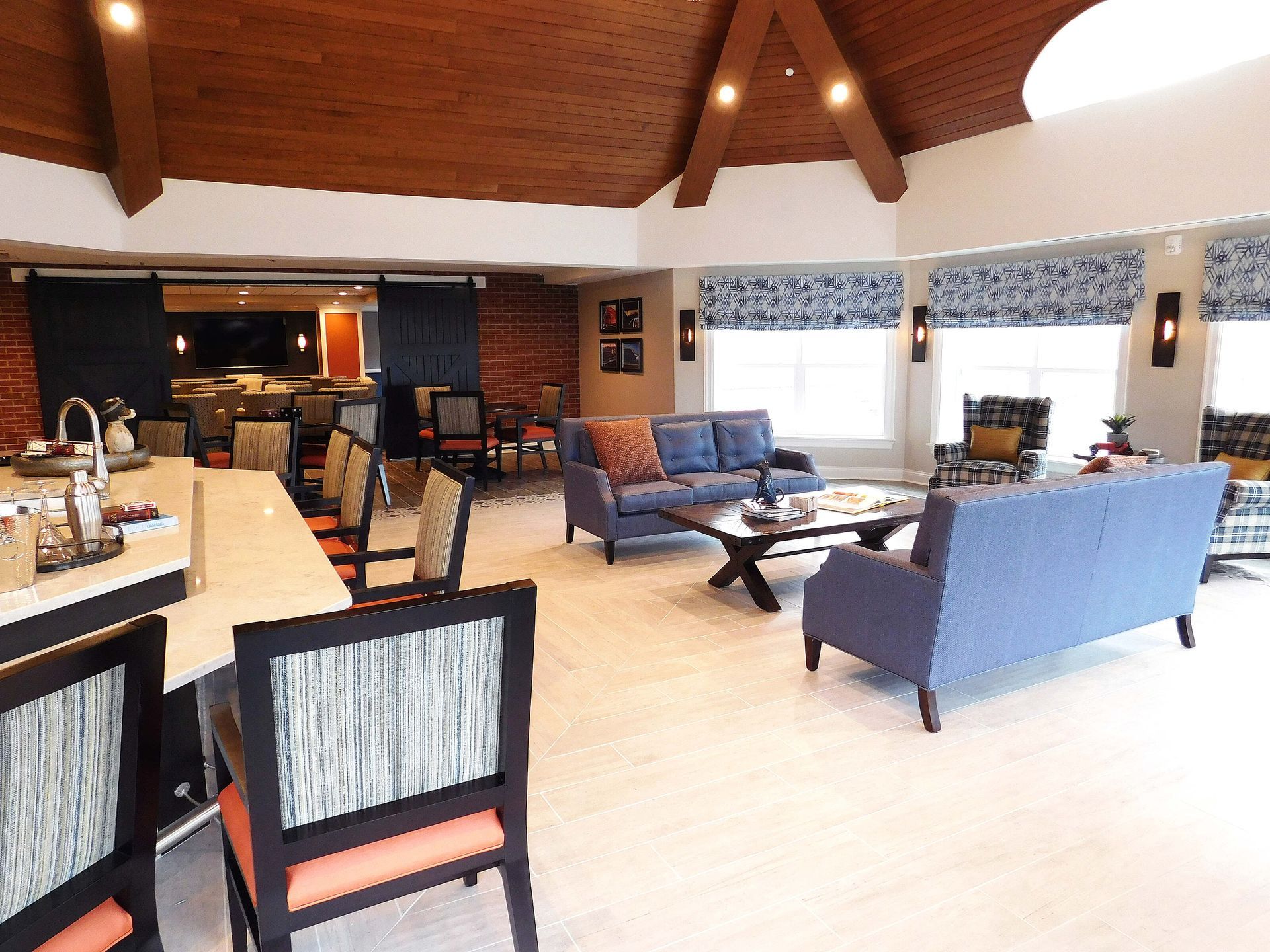 Modern living room with vaulted wooden ceiling, blue sofas, and a long bar counter with stools