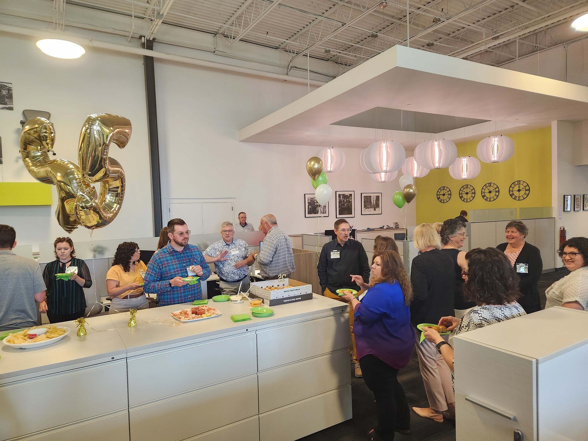 People gathered at a decorated indoor event table with balloons and snacks in a bright room.