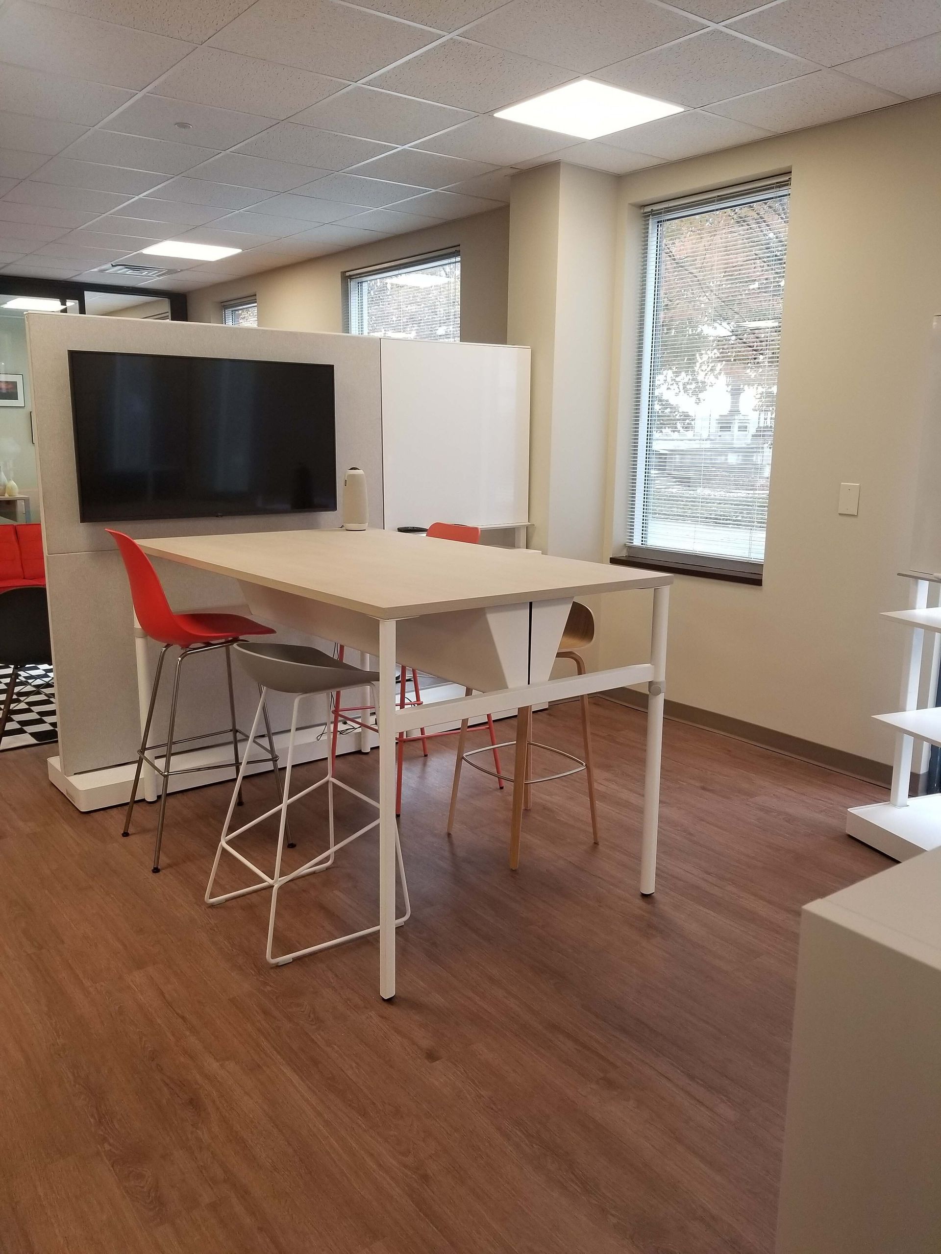Open office lounge with a TV, white table, red chair, and wood flooring.