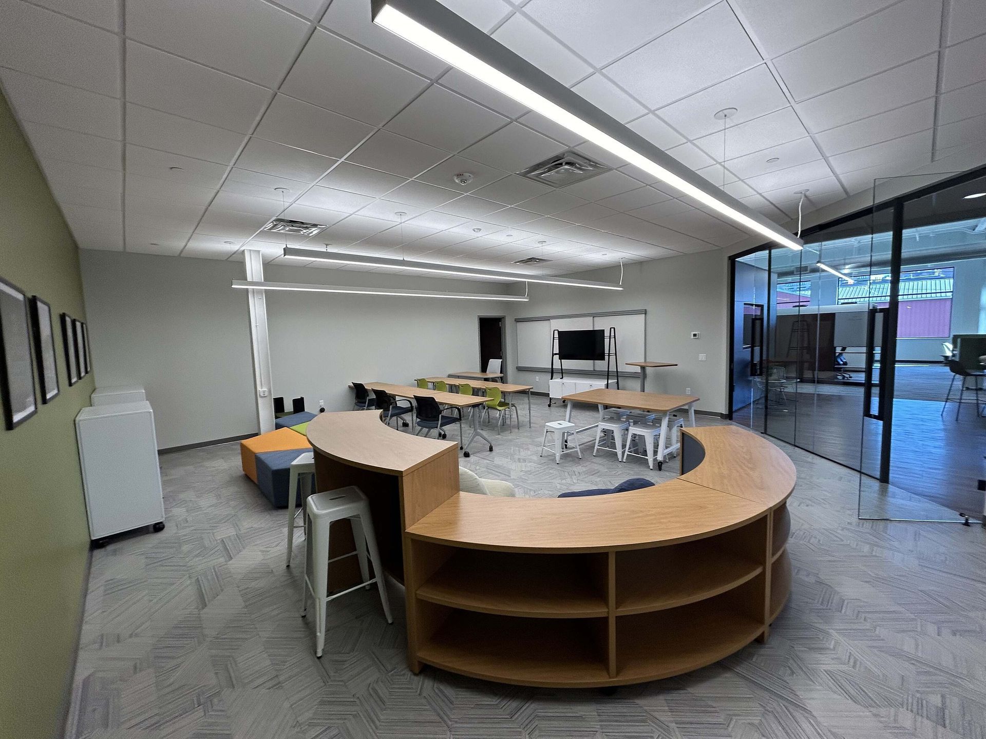 Empty modern meeting room with curved wooden desk, tables, chairs, and glass wall to hallway