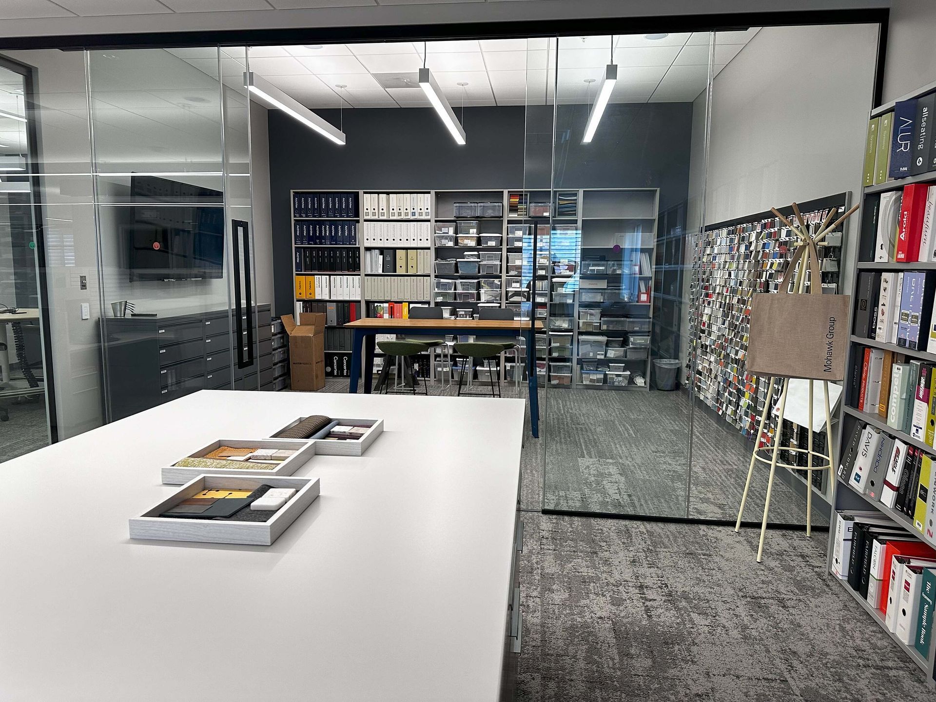 Modern library with white table, bookshelves, glass wall, and a work area in the background