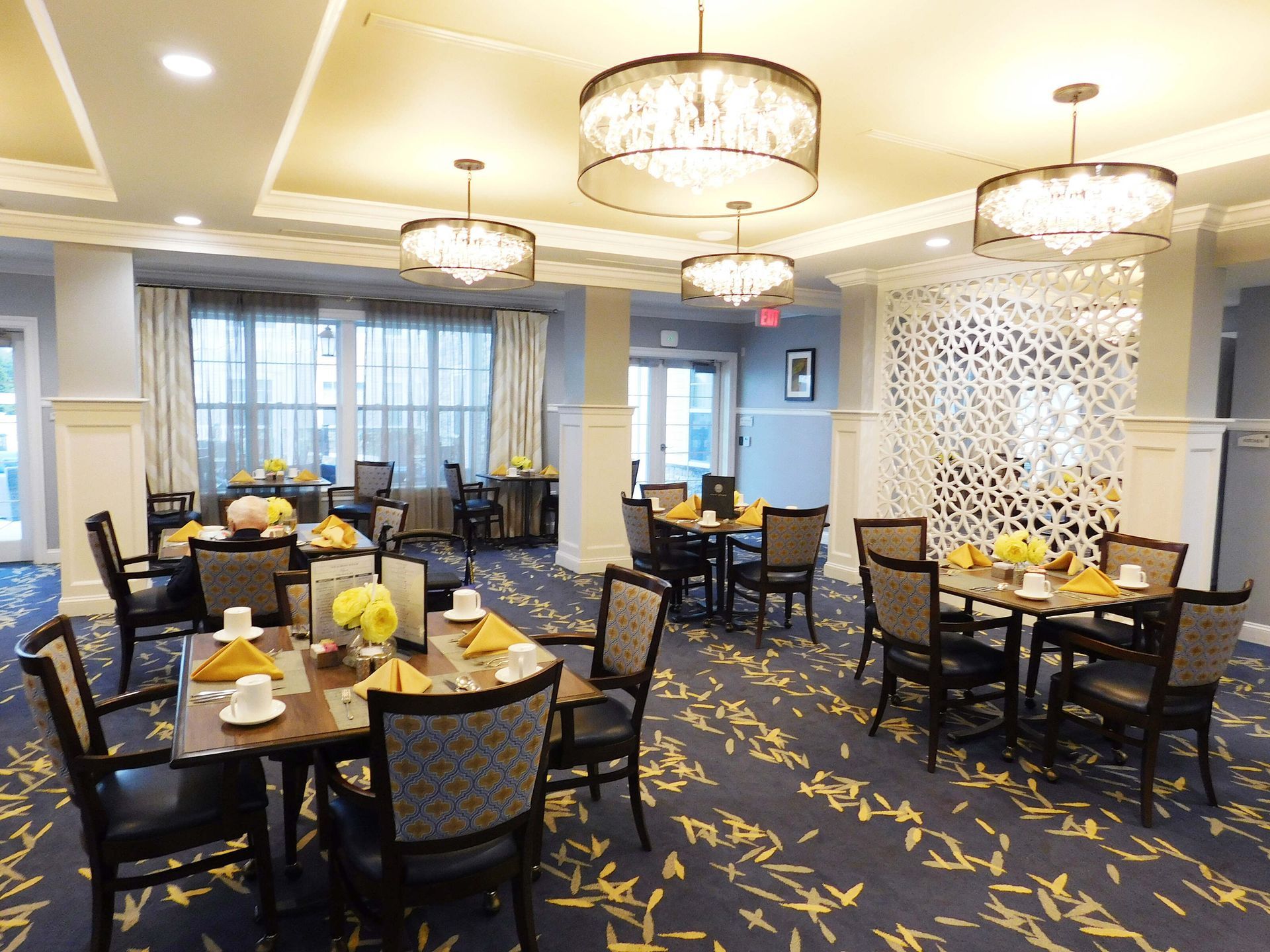 Elegant hotel dining room with round tables, black chairs, chandeliers, and patterned carpet