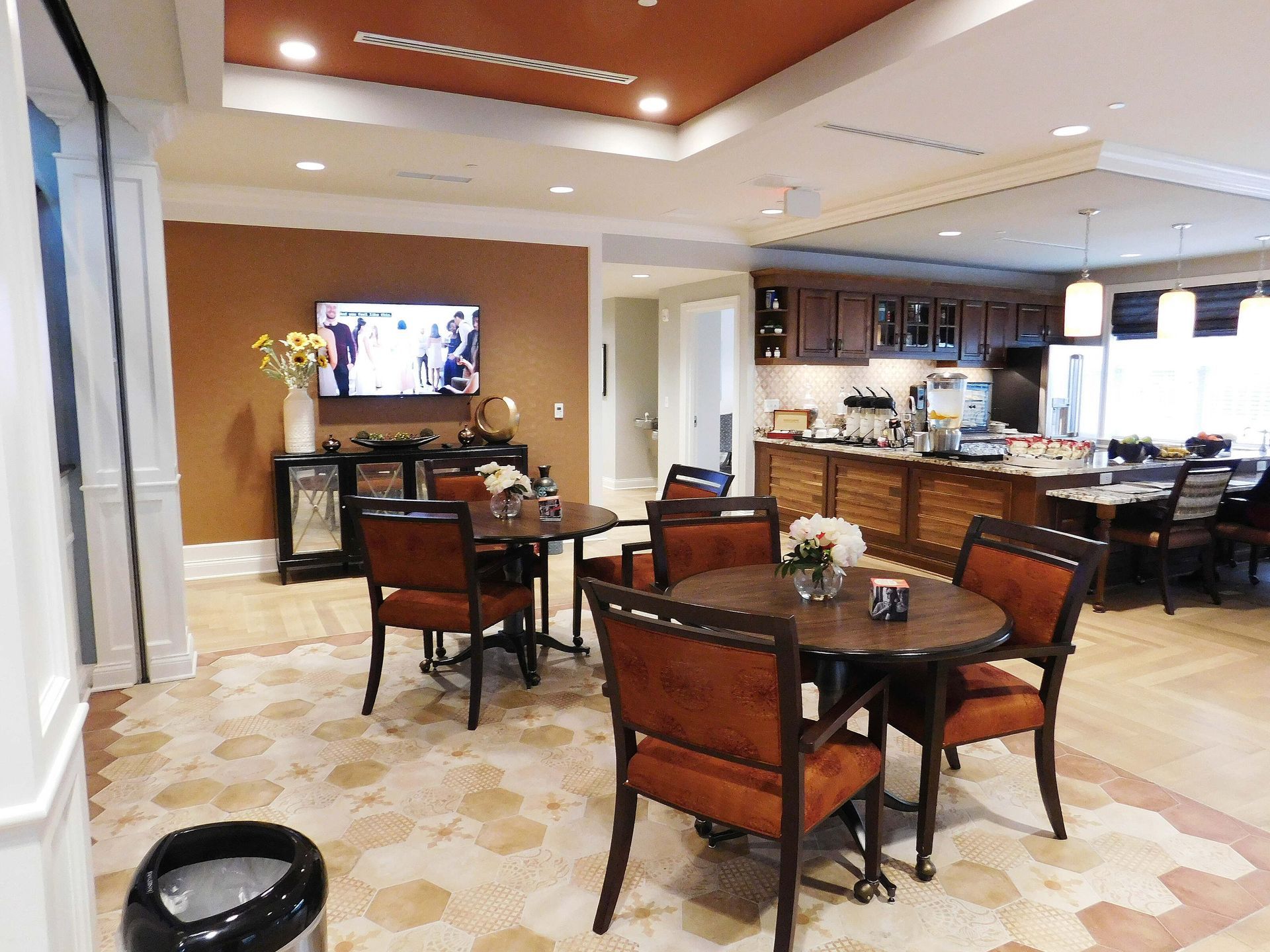 Modern dining room with round tables, upholstered chairs, and a kitchen/bar in the background.