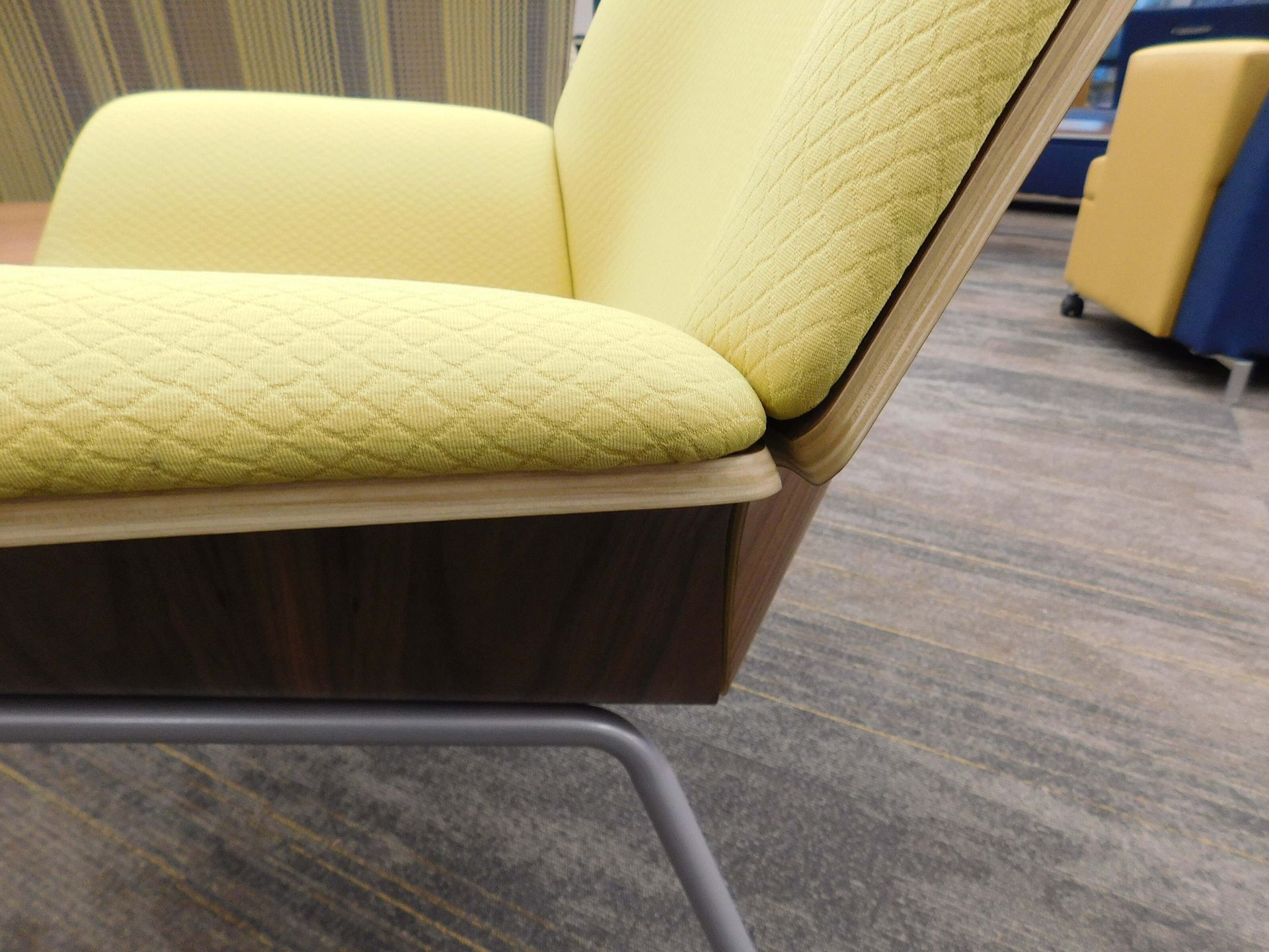 Yellow upholstered chair with wooden base and metal legs in a lounge area