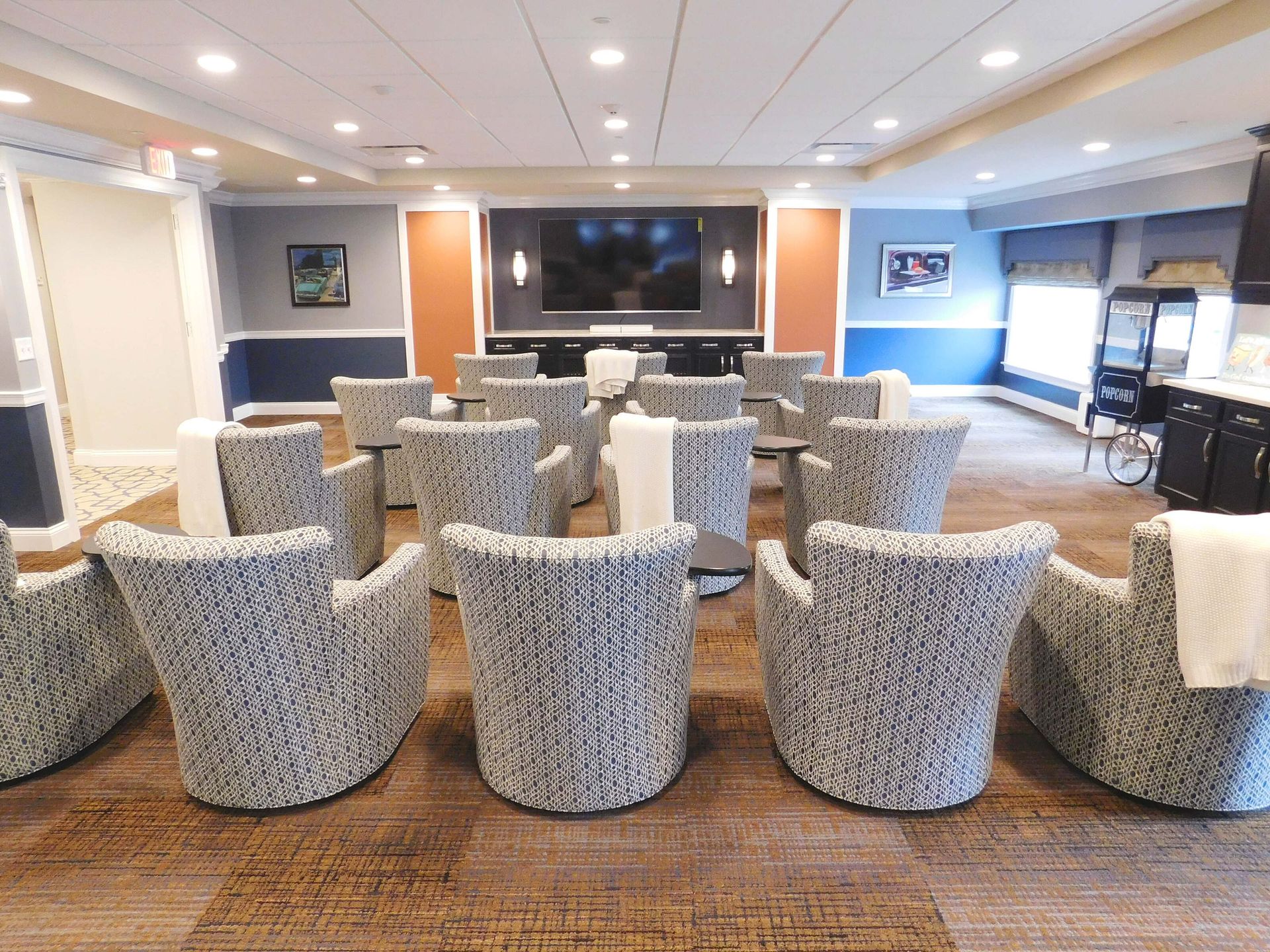 Modern lounge with patterned armchairs facing a large TV and fireplace in a bright, carpeted seating area