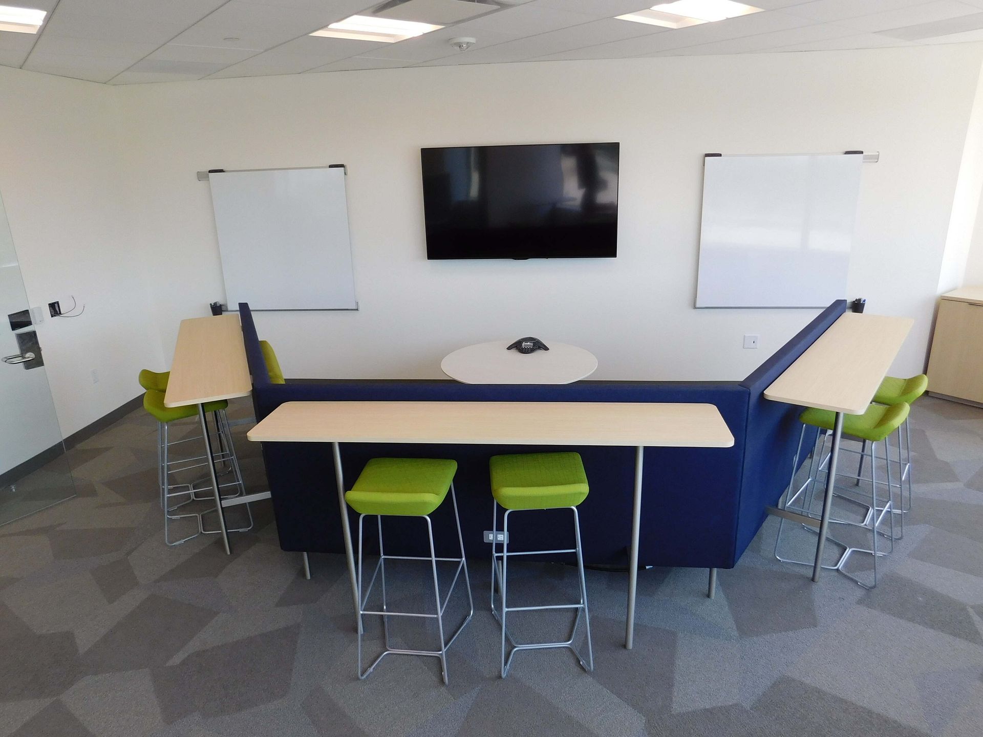 Small conference room with TV, whiteboards, blue table, and green stools.