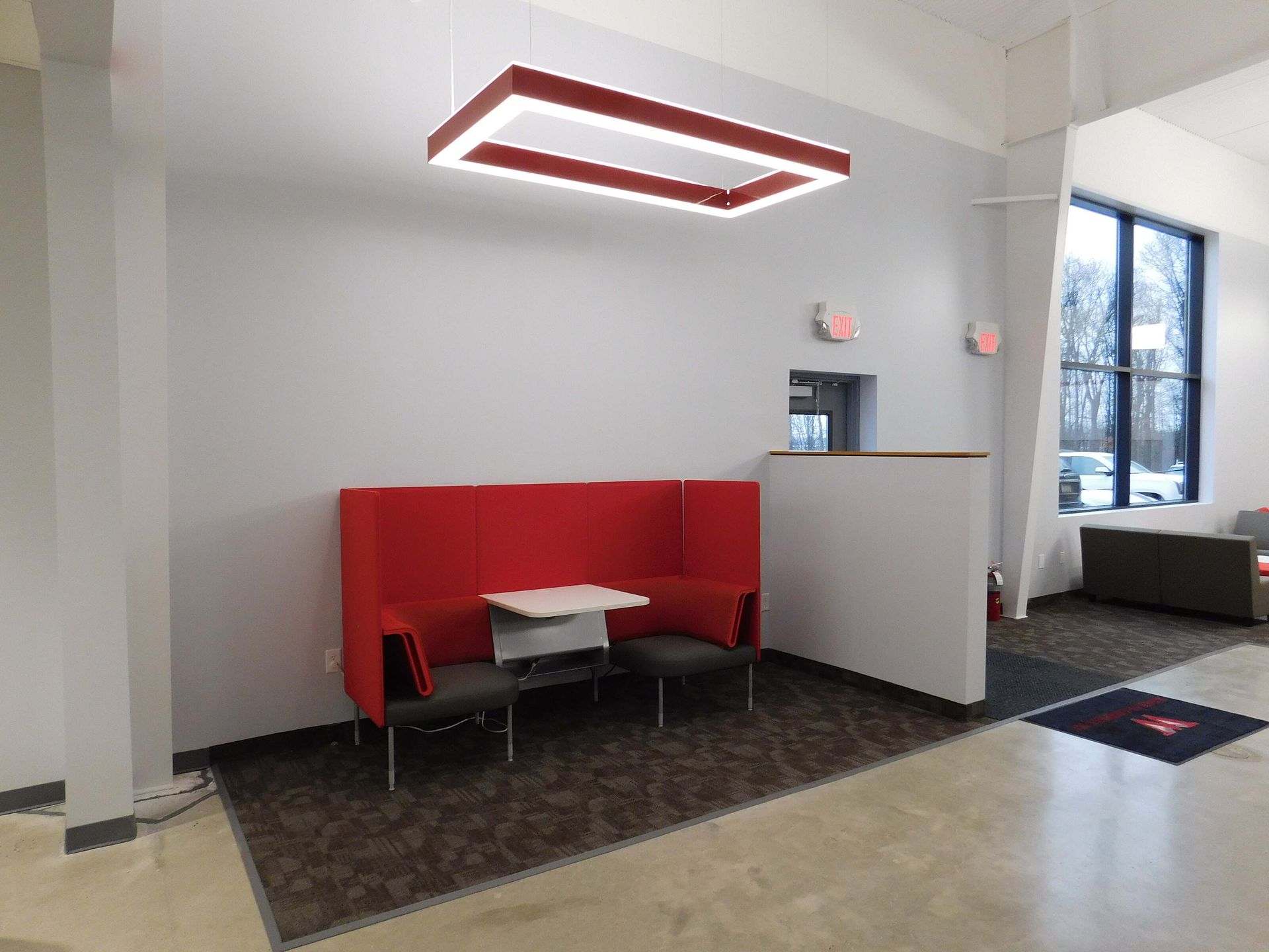 Modern lobby seating area with red booth, white walls, and a large window.