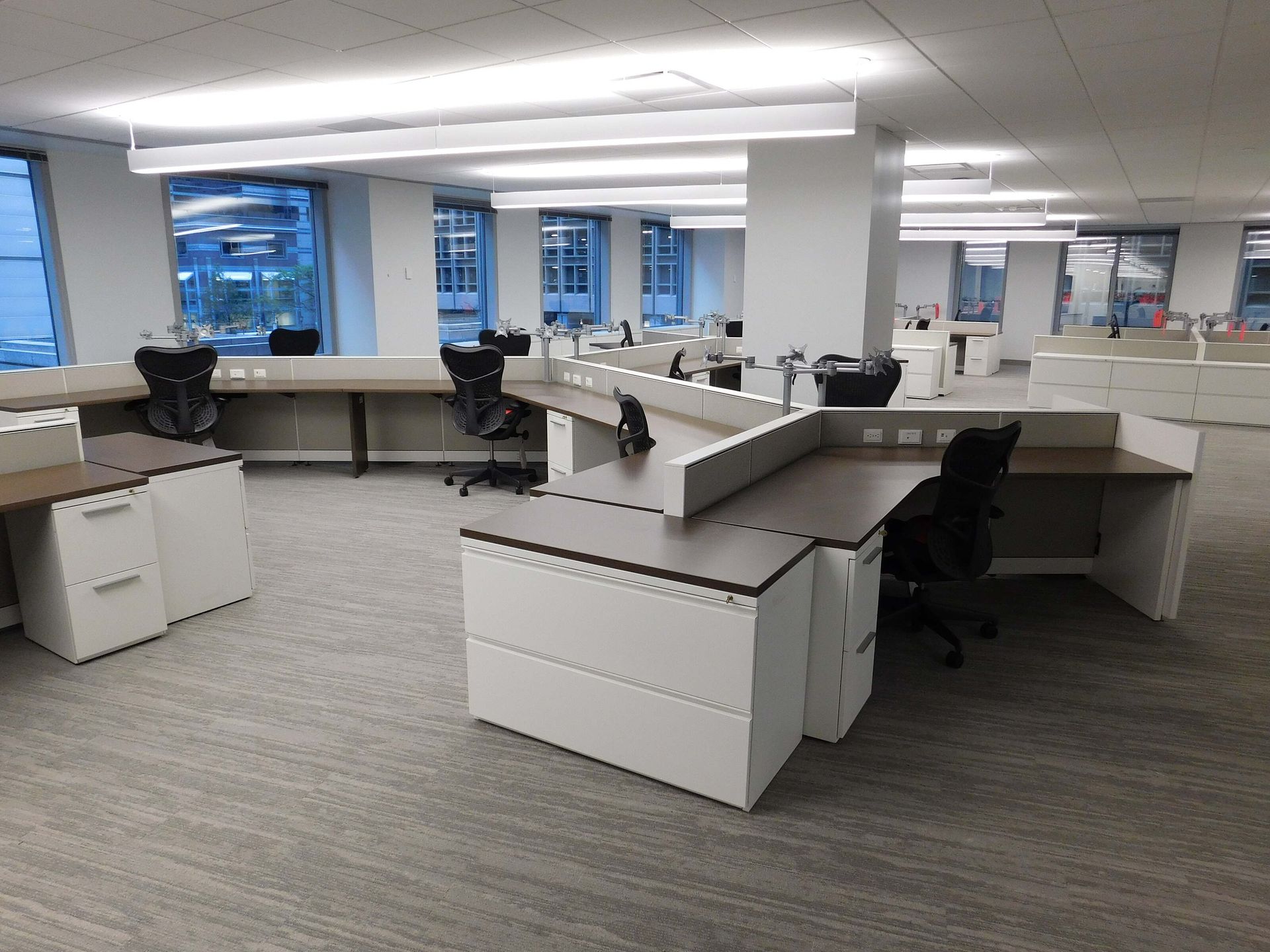 Empty open-plan office with white desks, black chairs, and large windows overlooking a cityscape