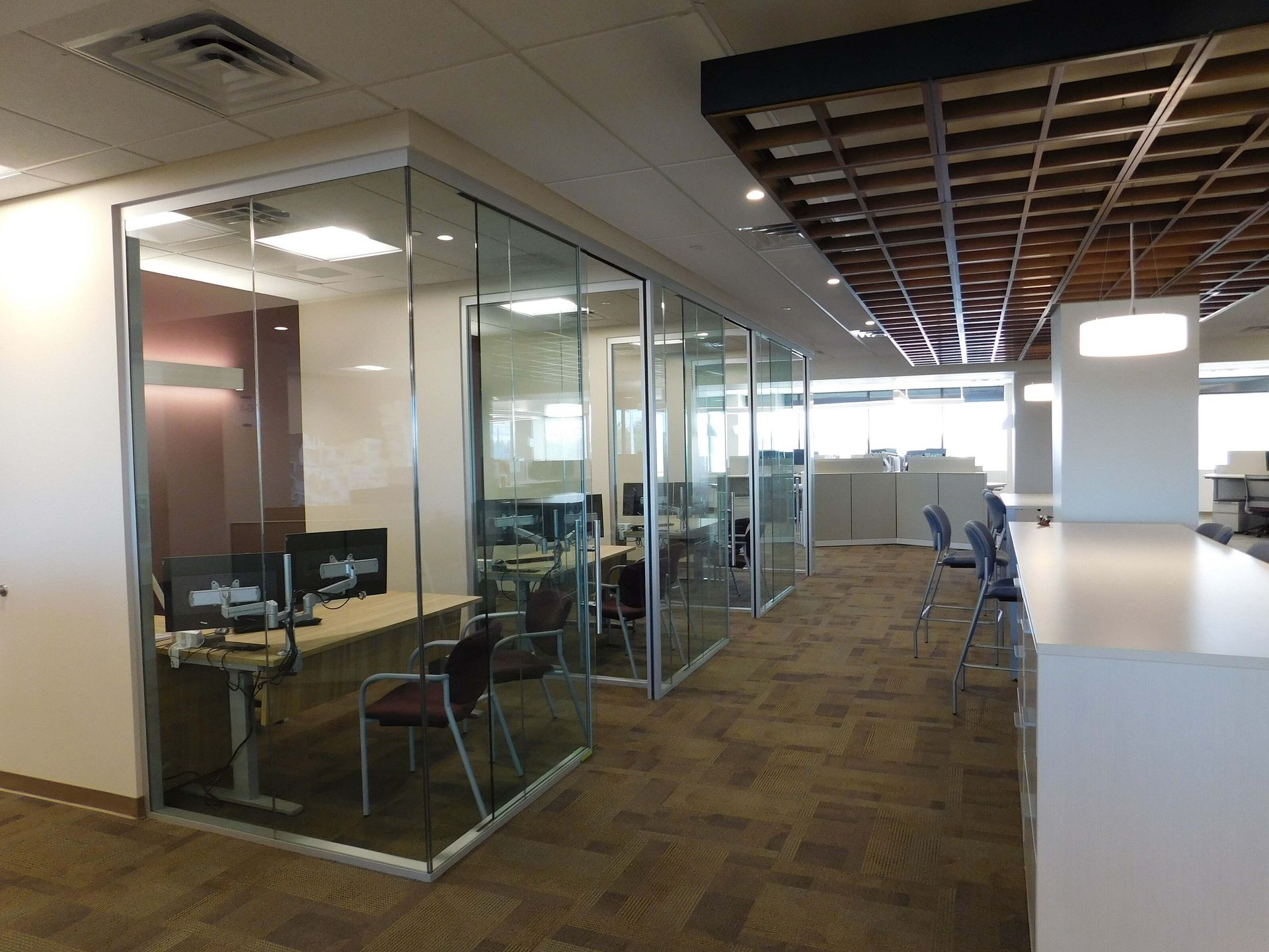 Modern office hallway with glass-walled meeting rooms, desks, and carpeted floor