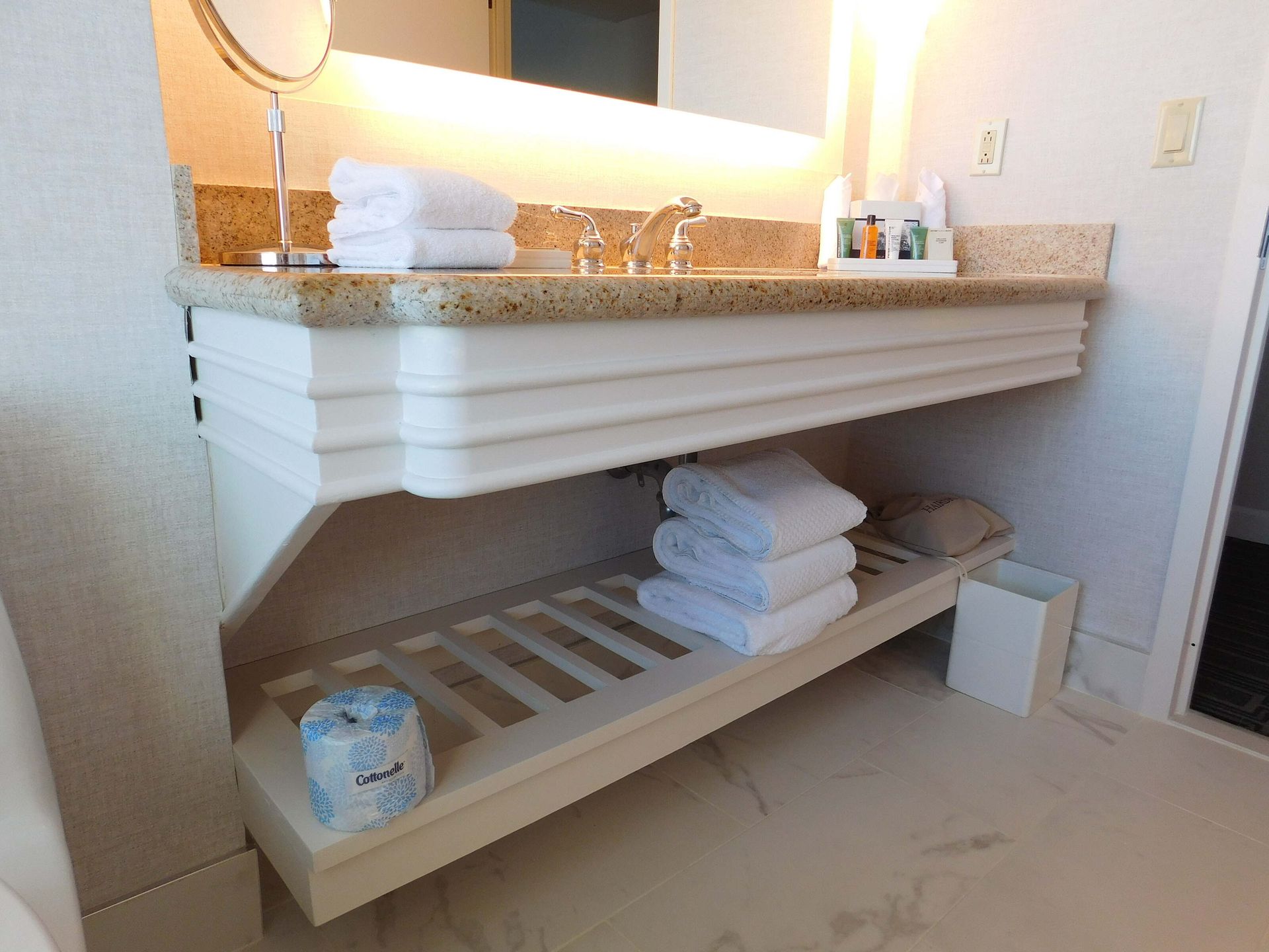 Bathroom vanity with granite countertop, vessel sink, towel shelf, and neatly folded white towels