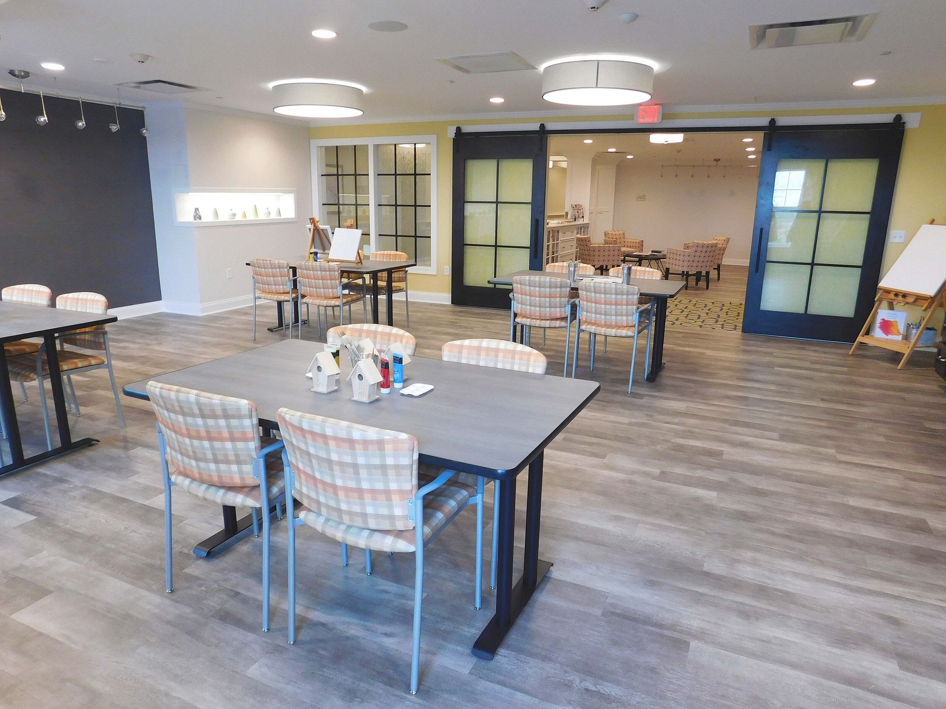 Empty dining room with gray tables, plaid chairs, and blue-framed doors on wood floors.