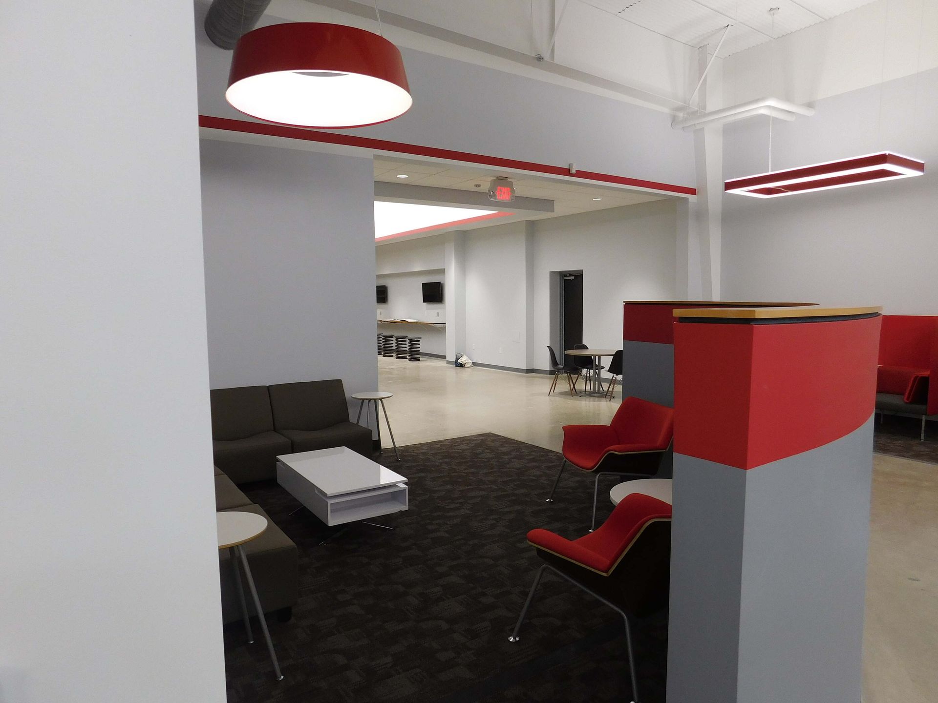 Modern lounge area with black chairs, red accents, and a white open office interior