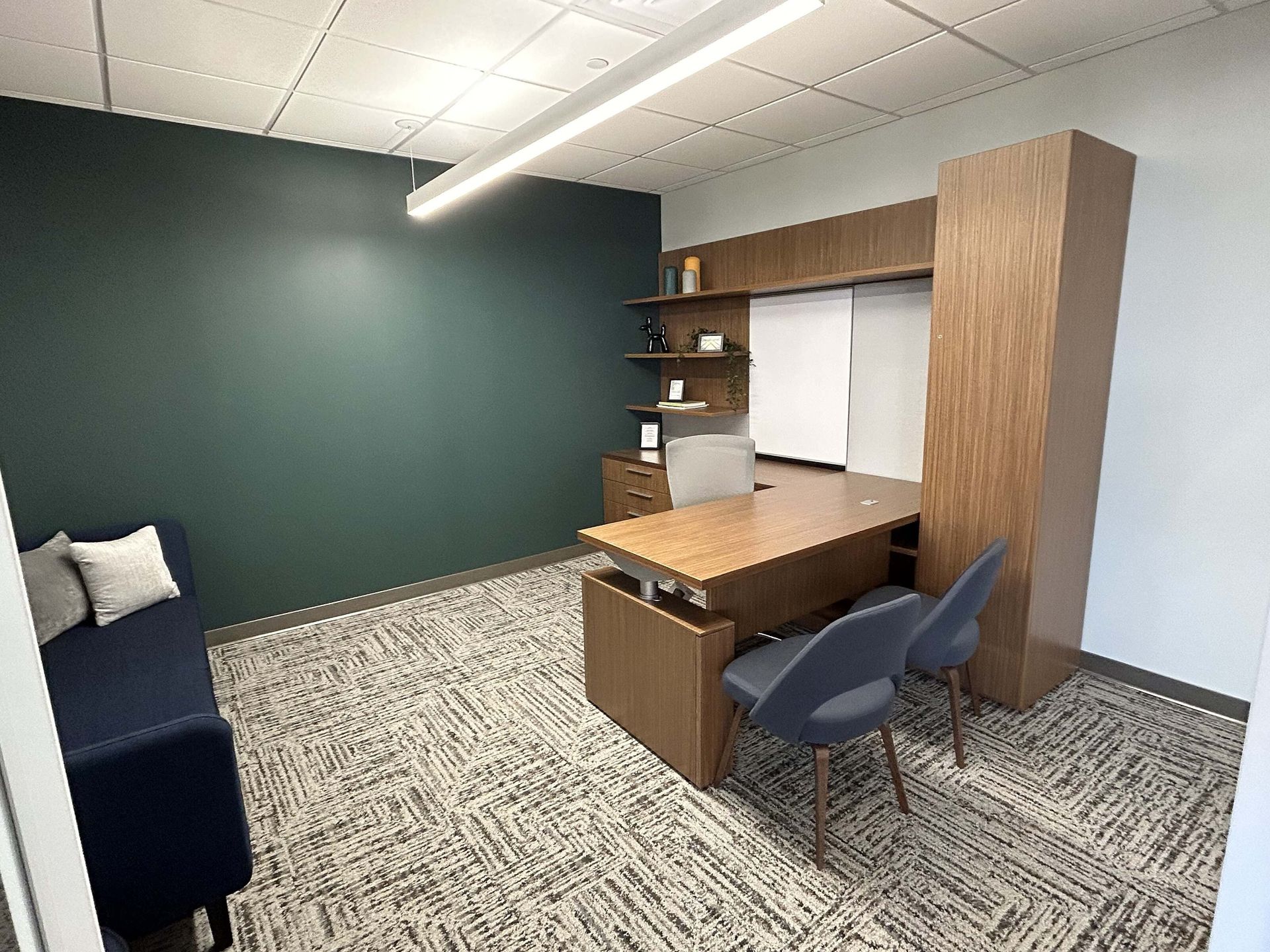Small modern office with a desk, blue chair, shelving, and dark green accent wall