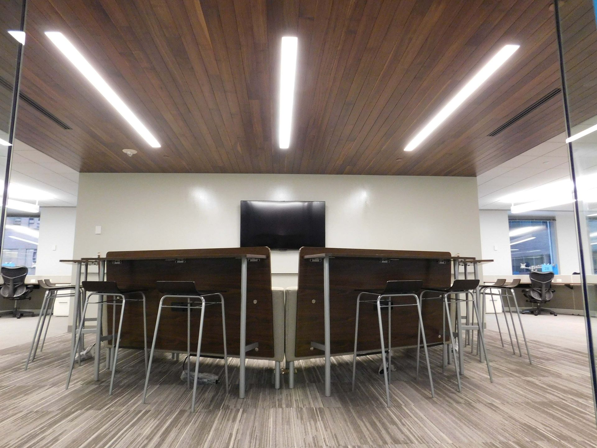 Modern conference room with a long table, stools, and overhead lights under a wood-paneled ceiling