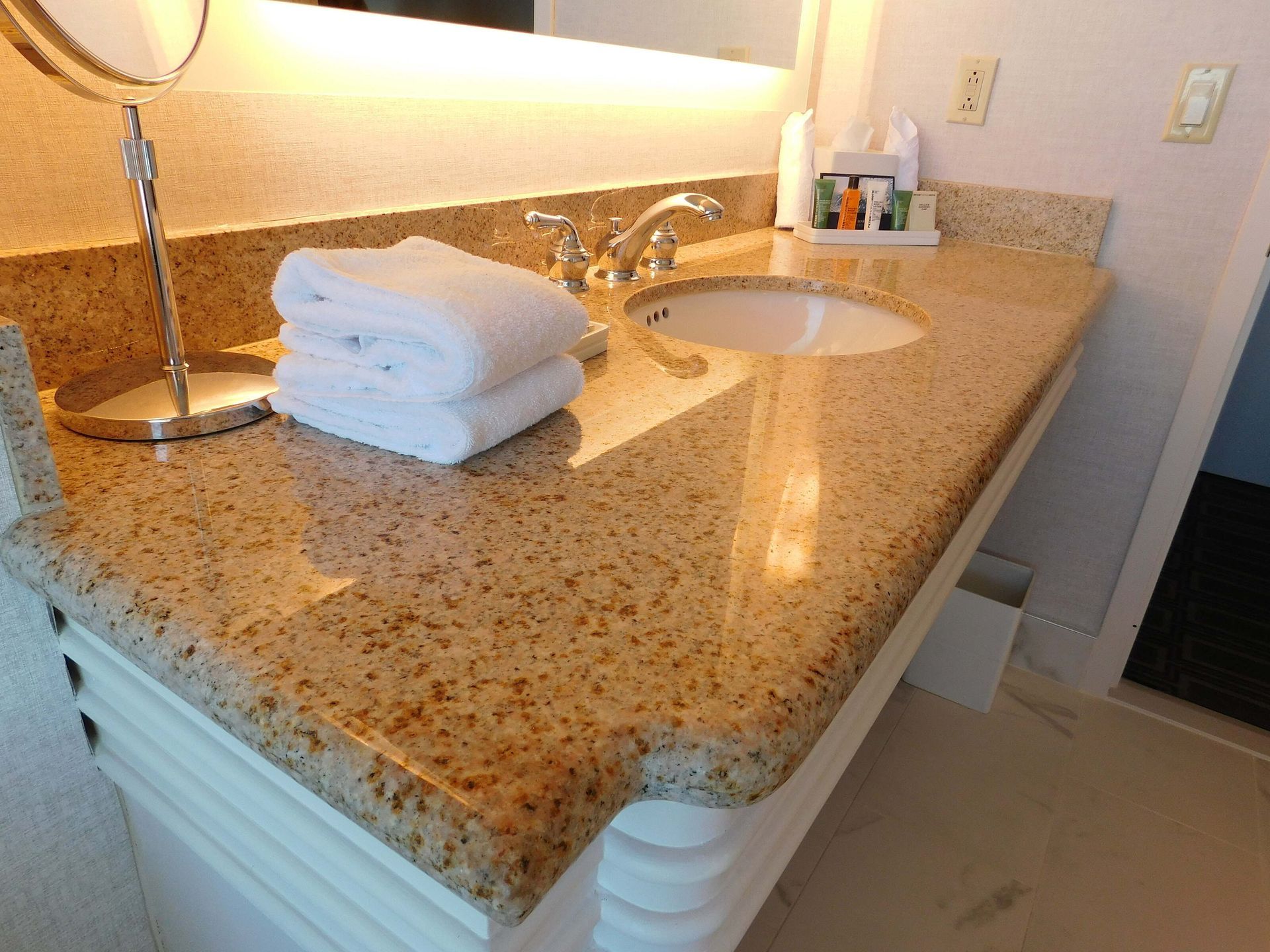 Bathroom vanity with granite countertop, sink, faucet, and folded white towels under warm lighting