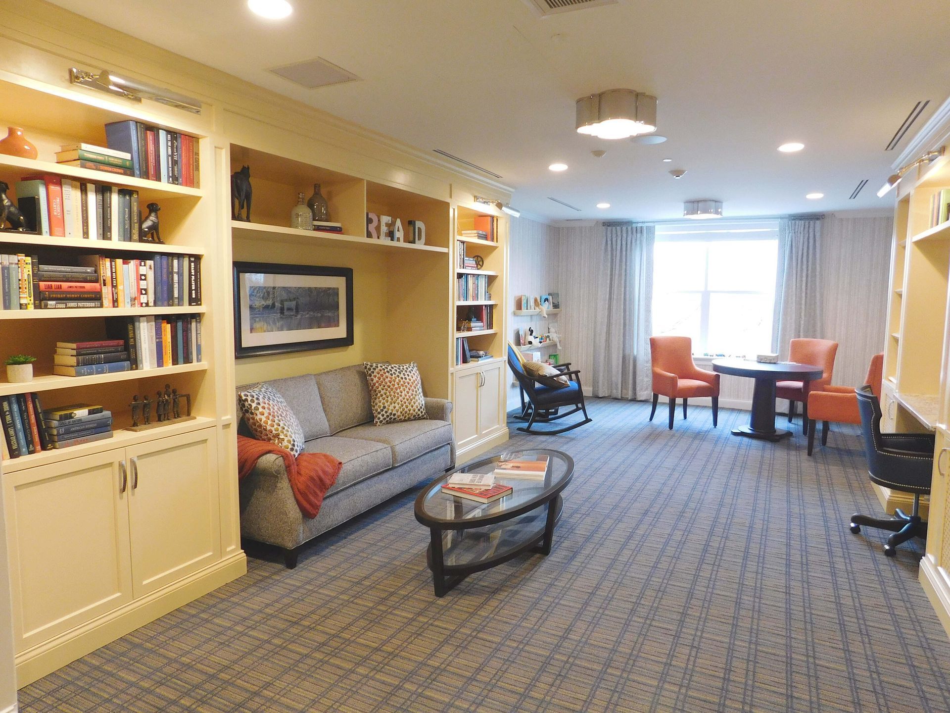 Cozy living room with bookshelves, sofa, chairs, coffee table, and a bright window at the back