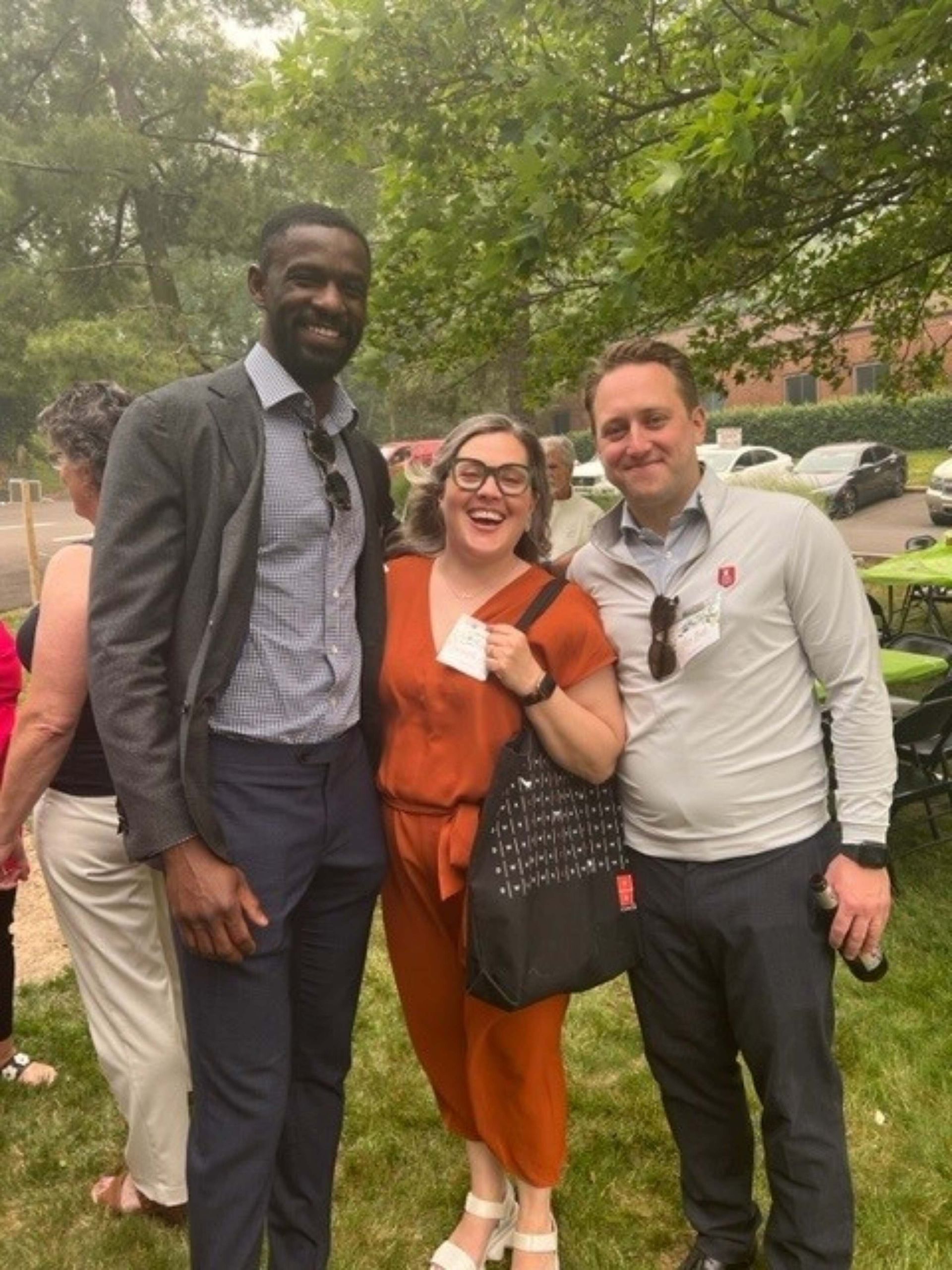 Three people smiling outdoors in a park, standing close together and posing for a photo.