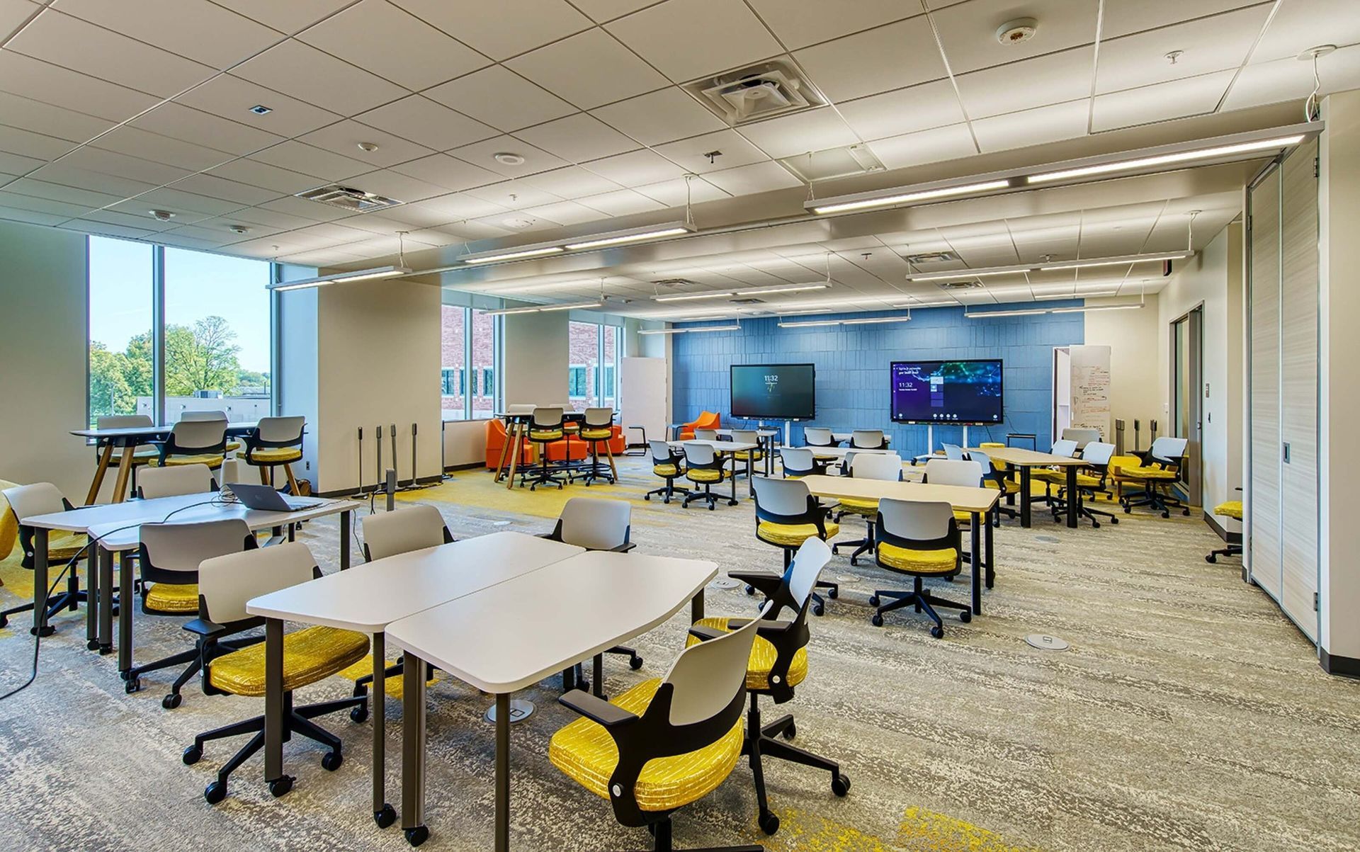 Bright modern classroom with tables, yellow chairs, and a large front display screen