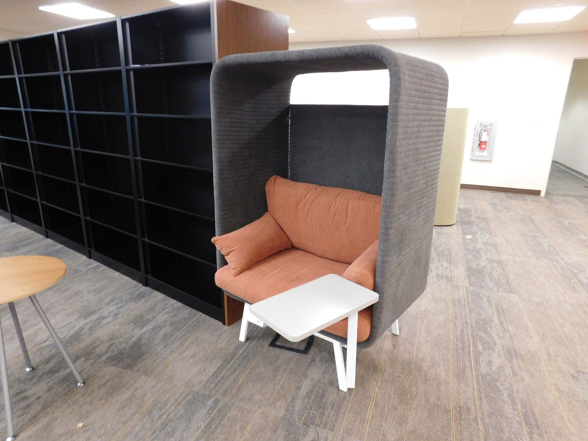 Cozy orange sofa nook in an office lounge beside black shelving and a small white table.