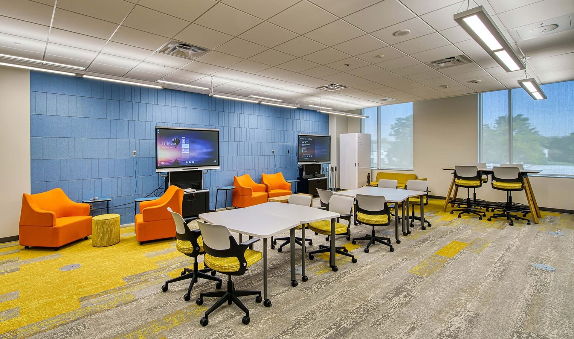 Modern office lounge with orange chairs, white tables, blue wall, and a TV screen