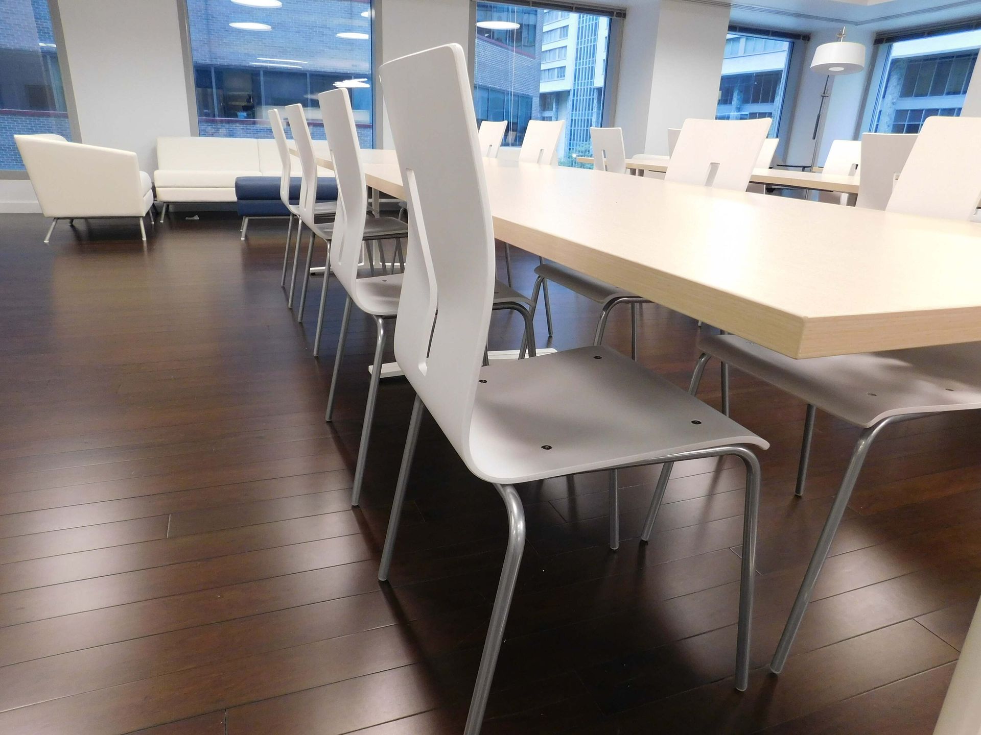 Modern office conference room with white chairs around a long table and dark wood floors