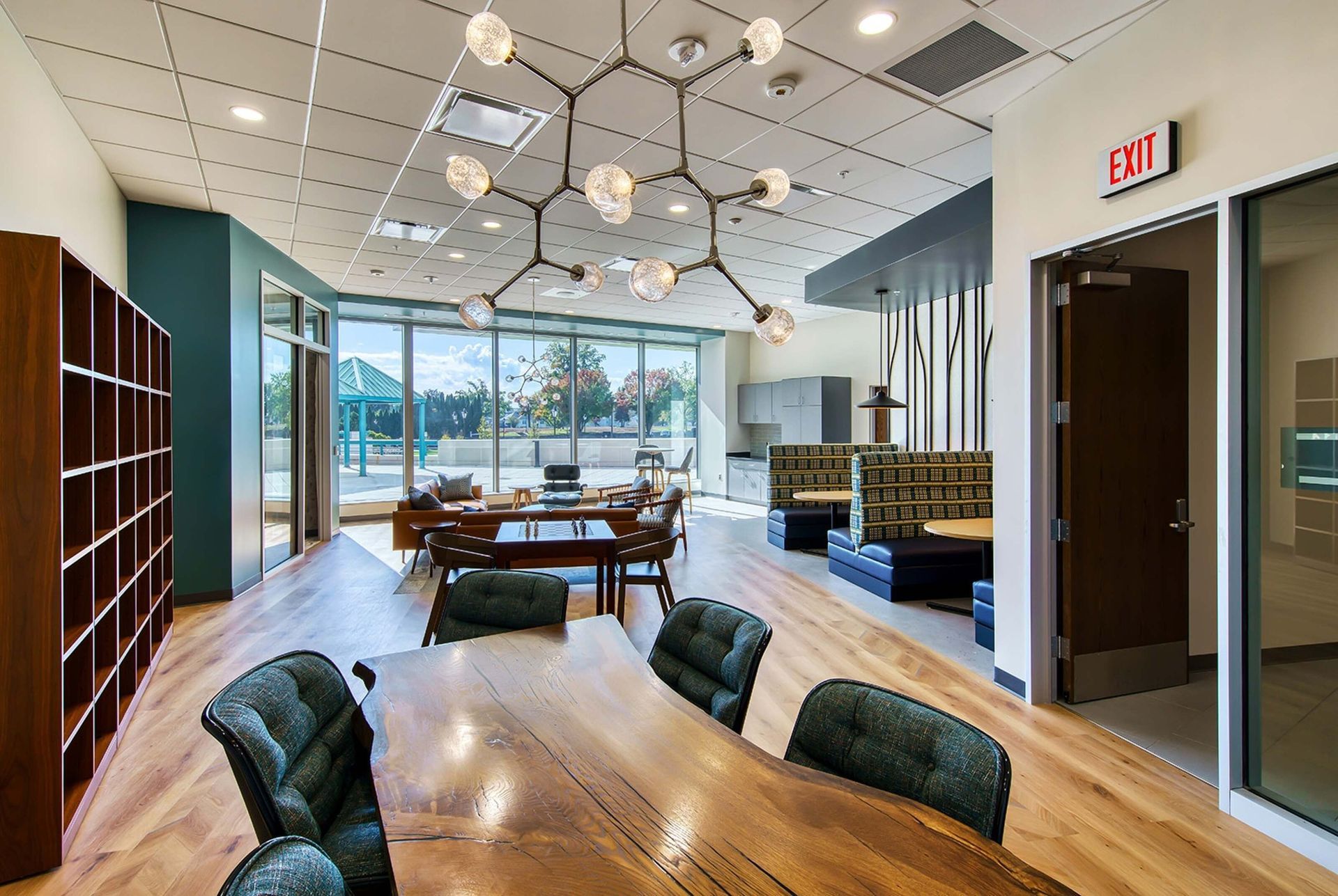 Modern office lounge with wood tables, green chairs, pendant lights, and glass walls overlooking outdoors