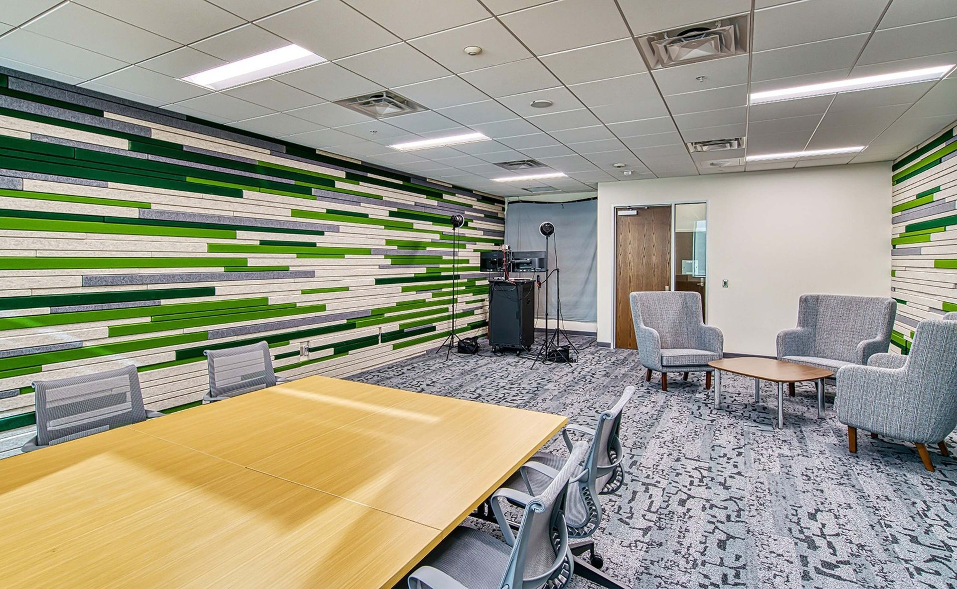 Modern office lounge with patterned carpet, round table, chairs, cabinets, and a green-striped accent wall