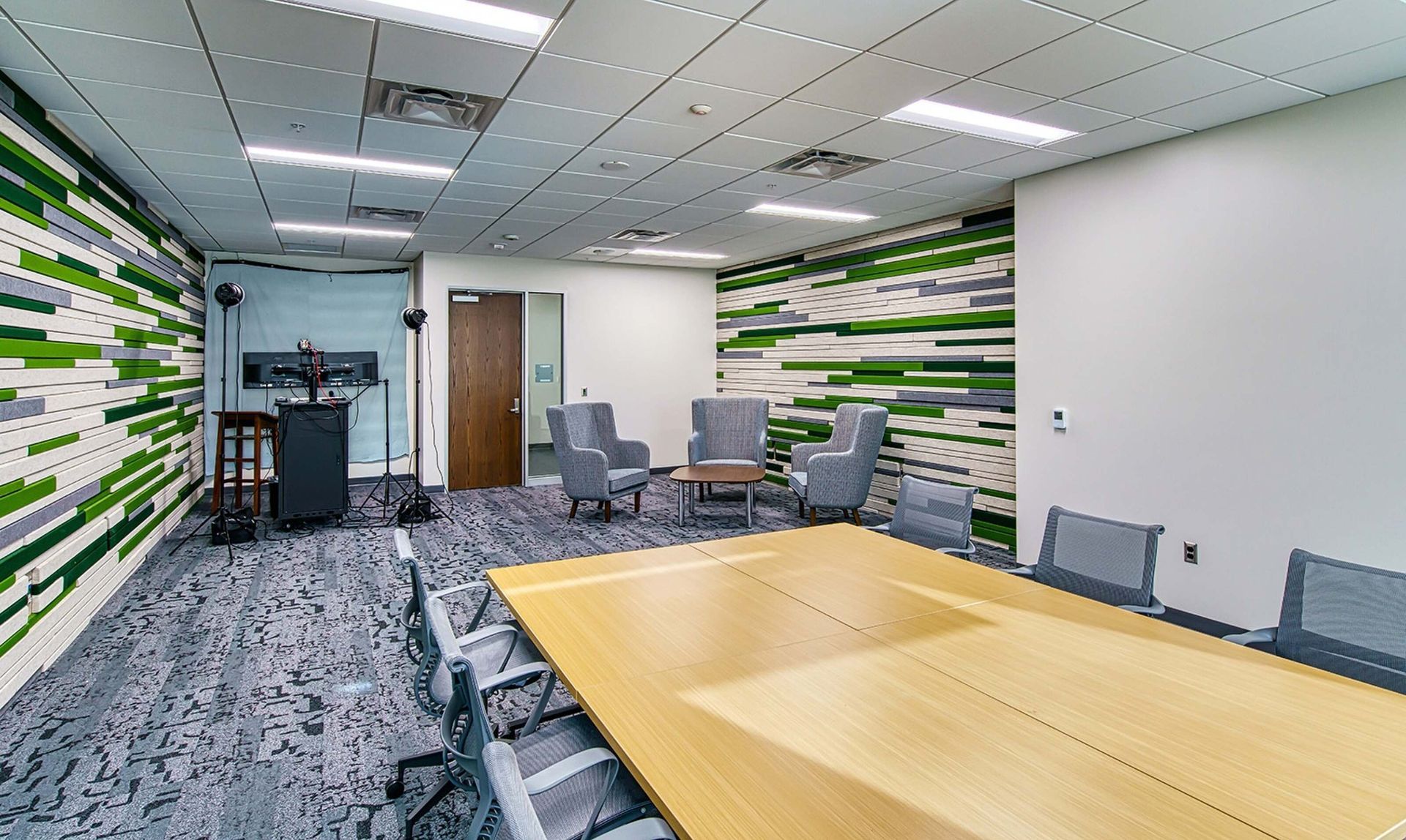Empty office conference room with long wooden table, gray chairs, and green-striped accent walls