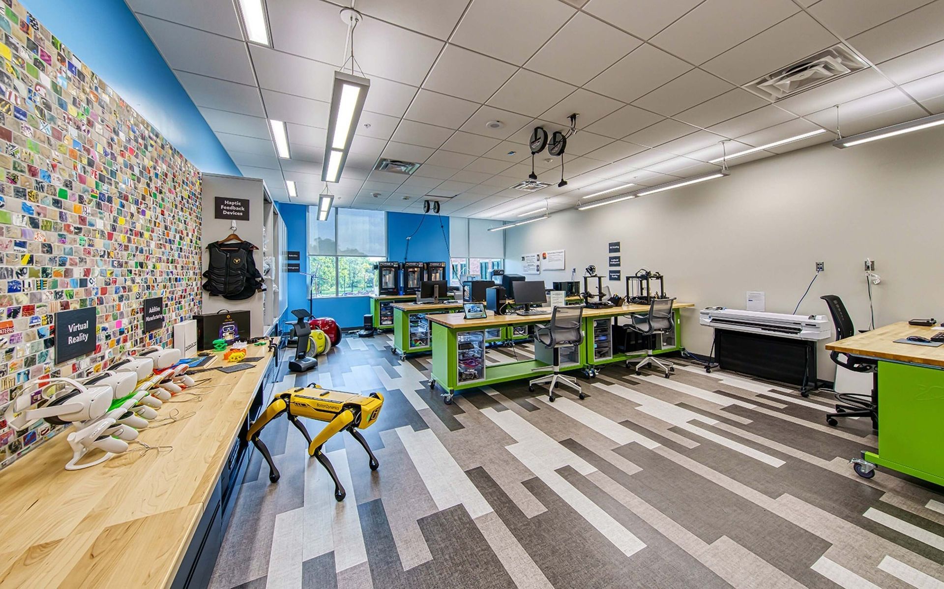 Bright maker space with worktables, tools, patterned wall, and colorful floor near large windows