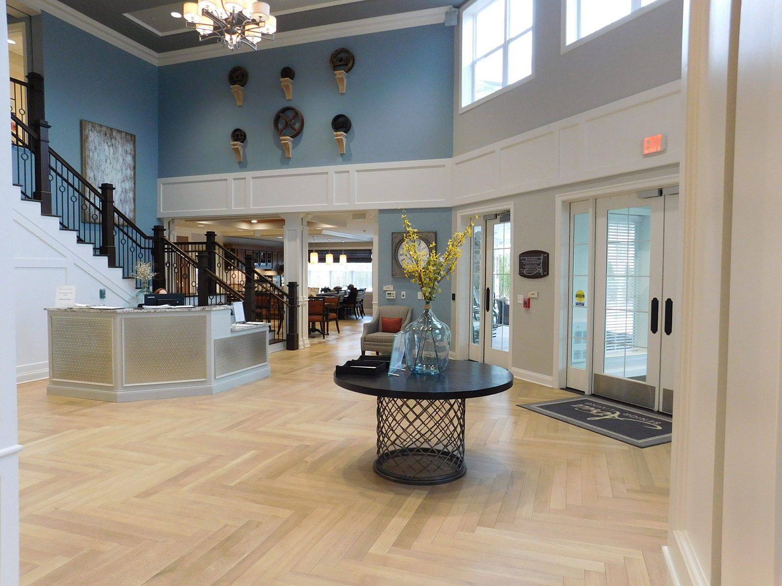 Bright hotel lobby with staircase, reception desk, blue walls, and herringbone wood floor