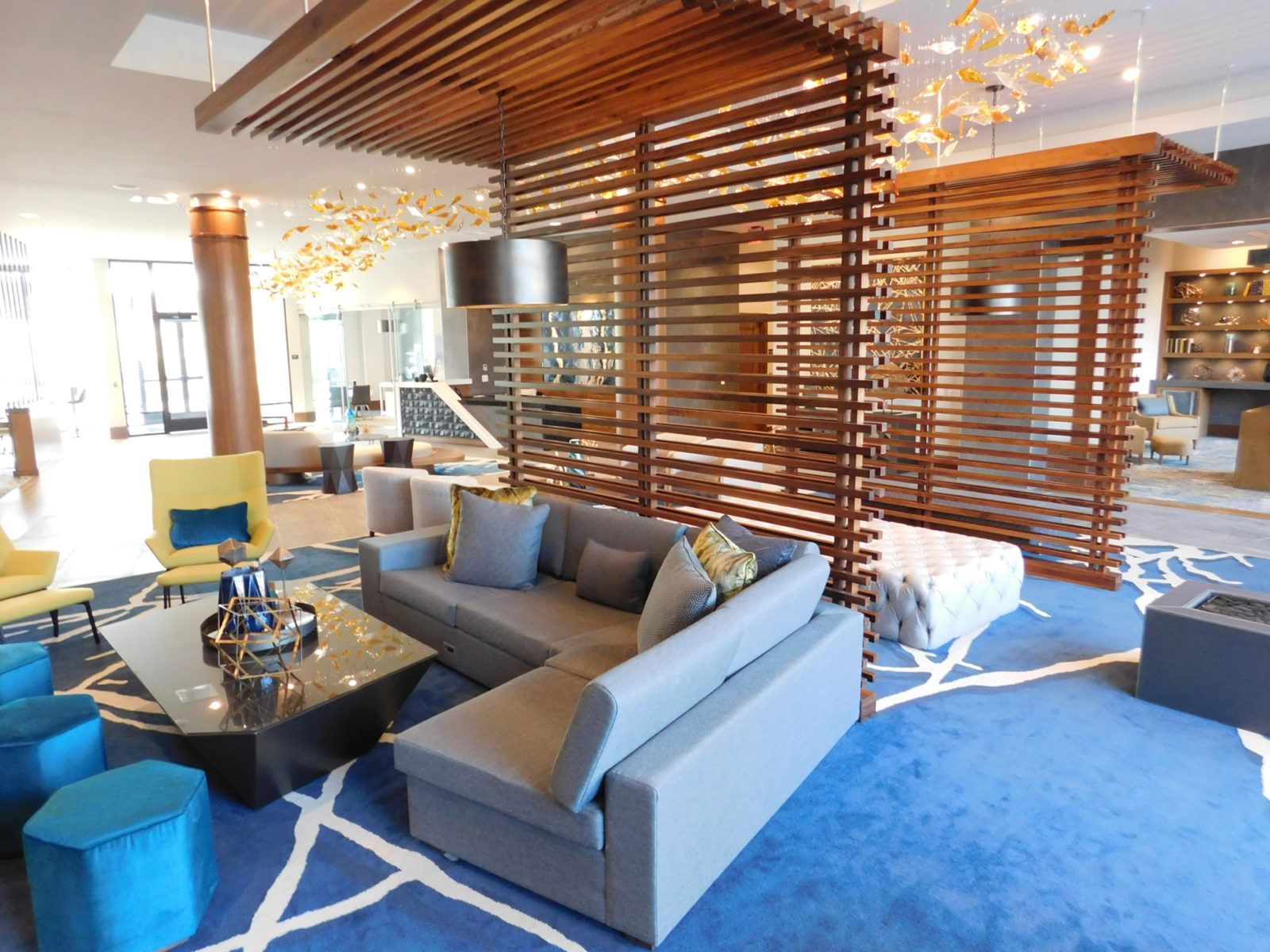 Modern living room with gray sofa, blue rug, wooden slat partitions, and hanging lights