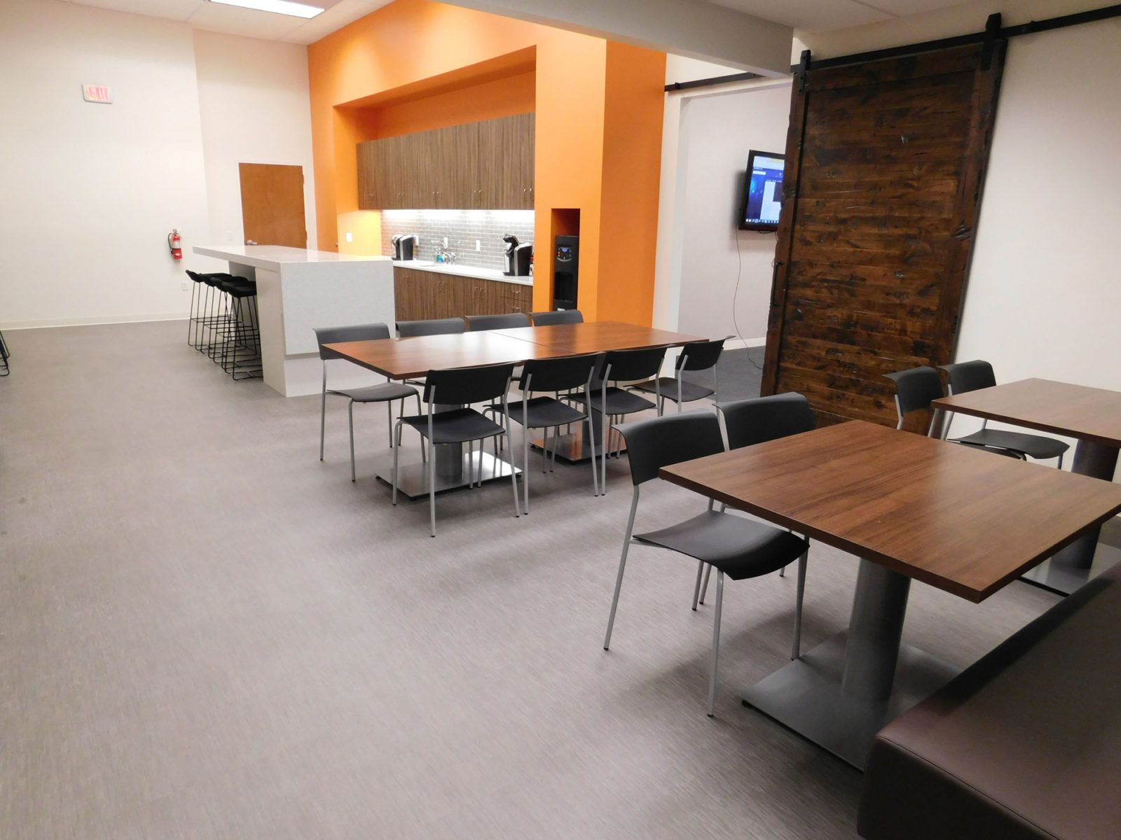 Empty modern cafeteria with wooden tables, black chairs, and an orange-accented counter area