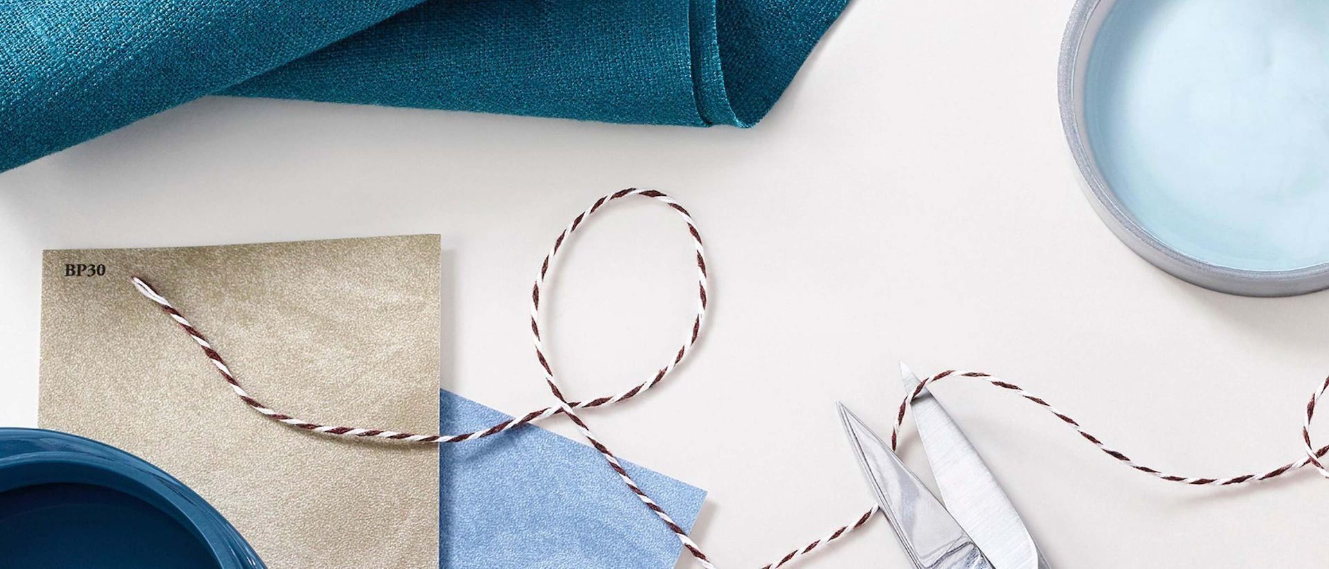 Craft materials on a white surface with blue paper, twine, and scissors
