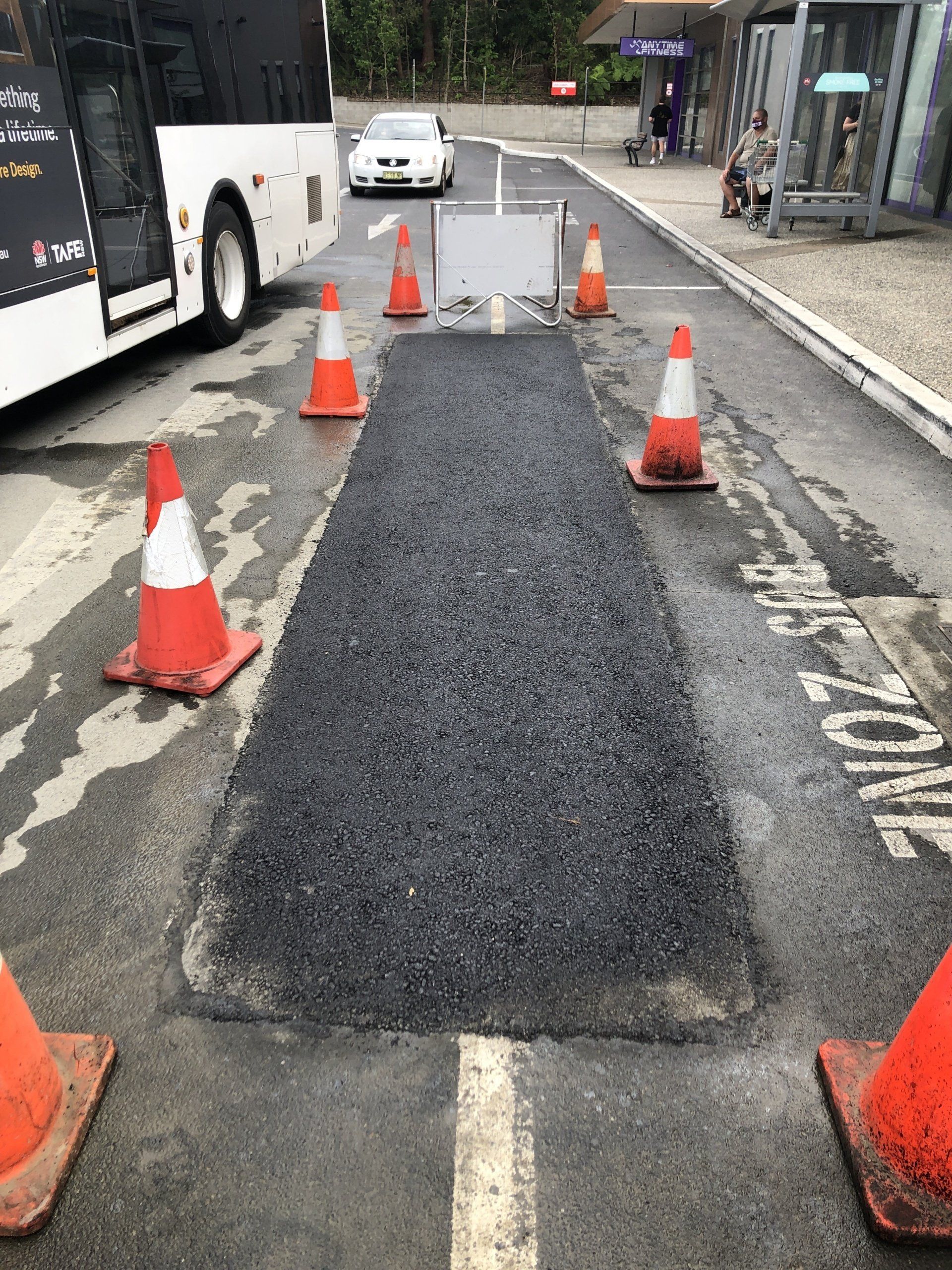 A bus is parked on the side of the road next to a patch of asphalt.