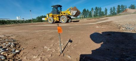 Obra en construcción con una cargadora amarilla en un camino de tierra bajo un cielo azul despejado.