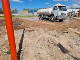 Camión cisterna blanco en una obra en construcción embarrada bajo un cielo azul despejado.