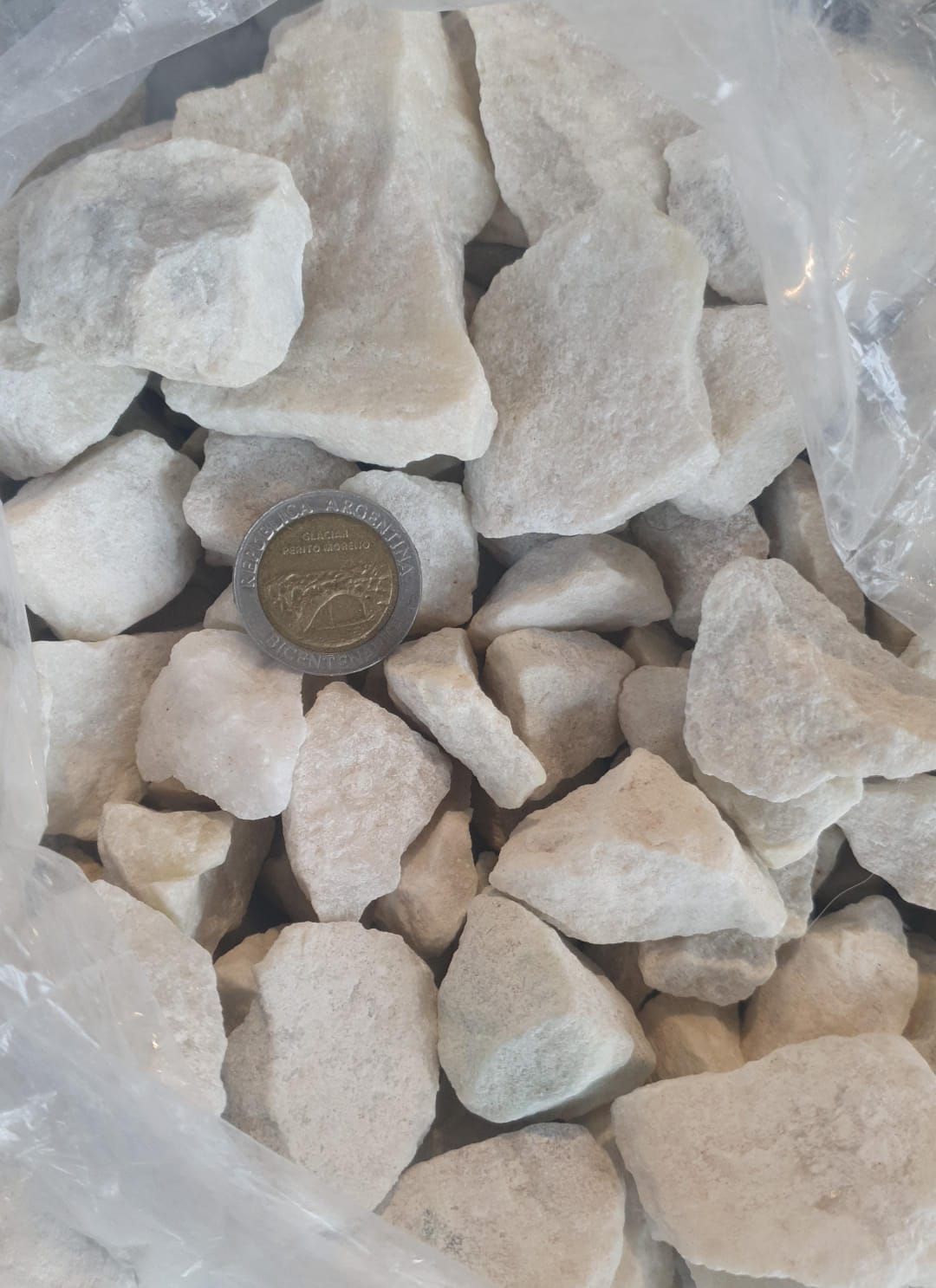 Montón de piedras de grava beige con una moneda para comparar el tamaño.