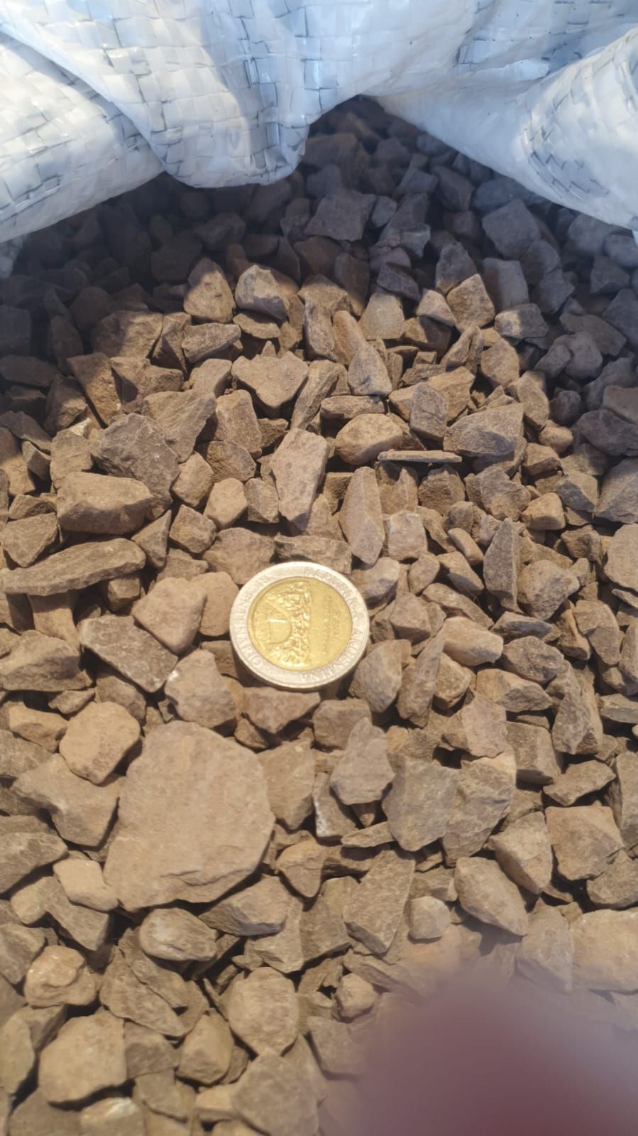 Montón de piedras marrones en un saco blanco con una pequeña tapa o tapón amarillo en el centro.