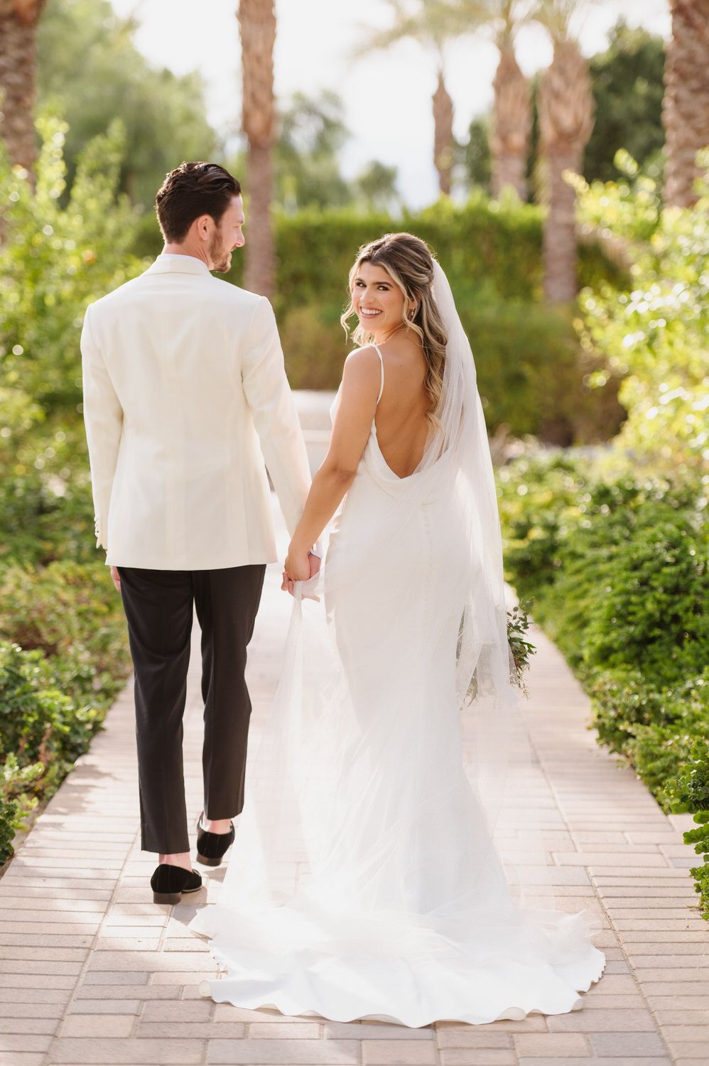 A bride and groom are walking down a path holding hands.