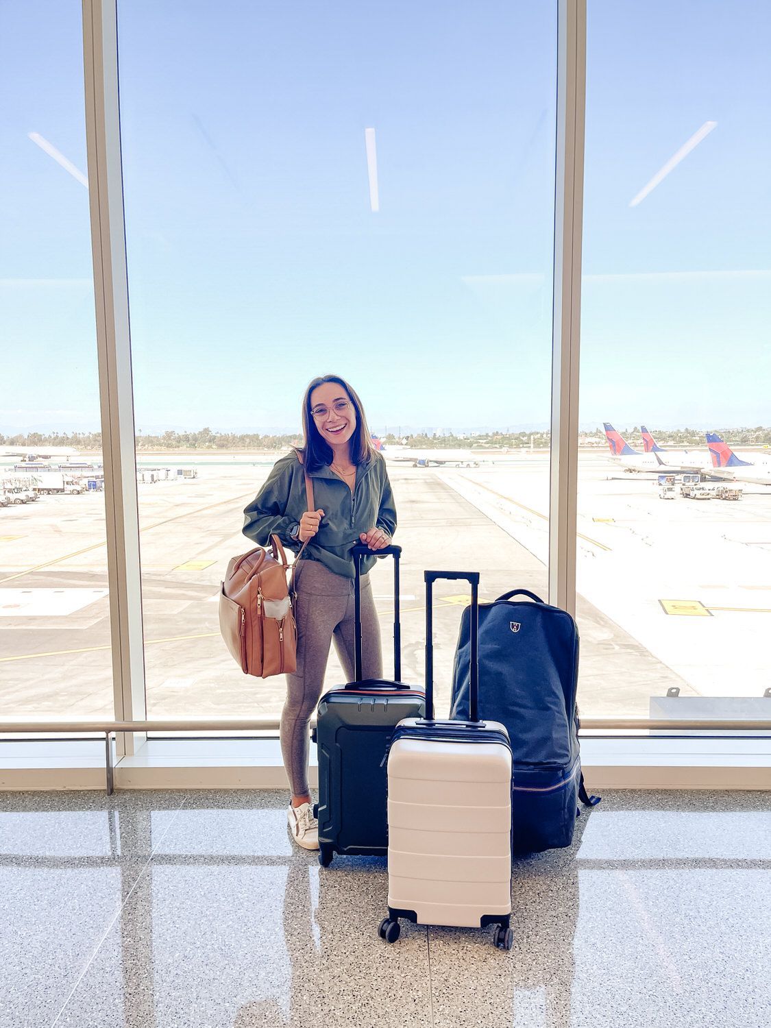 Traveler with luggage standing at an airport window, smiling in a bright terminal.